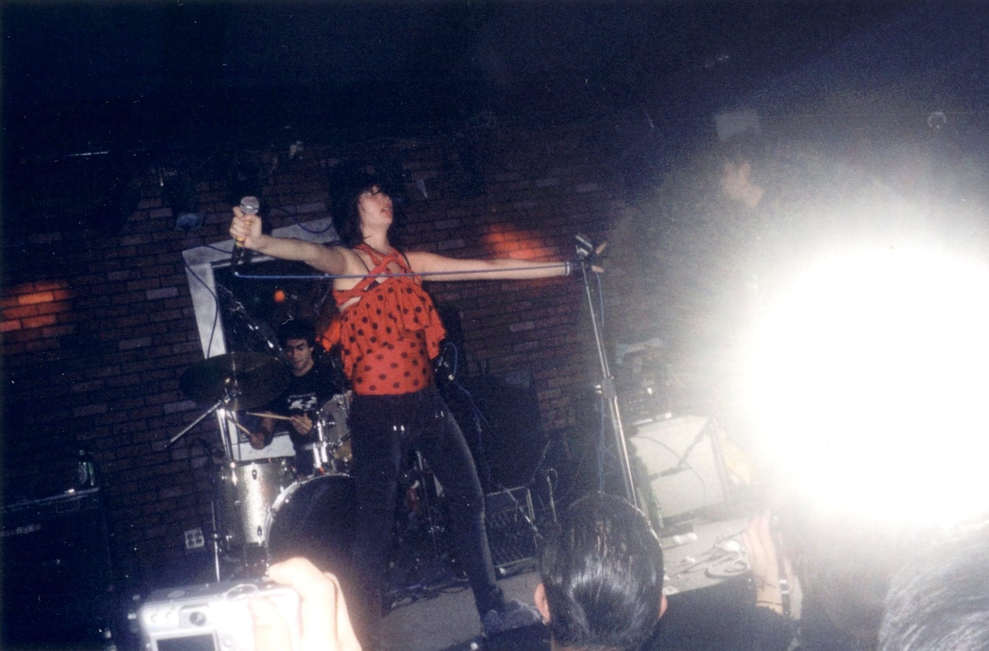 a woman in a red and black polka dotted top and black jeans holds a microphone while performing on stage