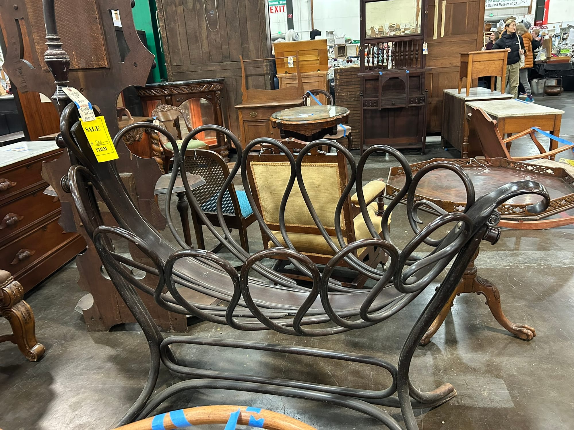 A large, brown wooden cradle sits surrounded by other pieces of vintage furniture