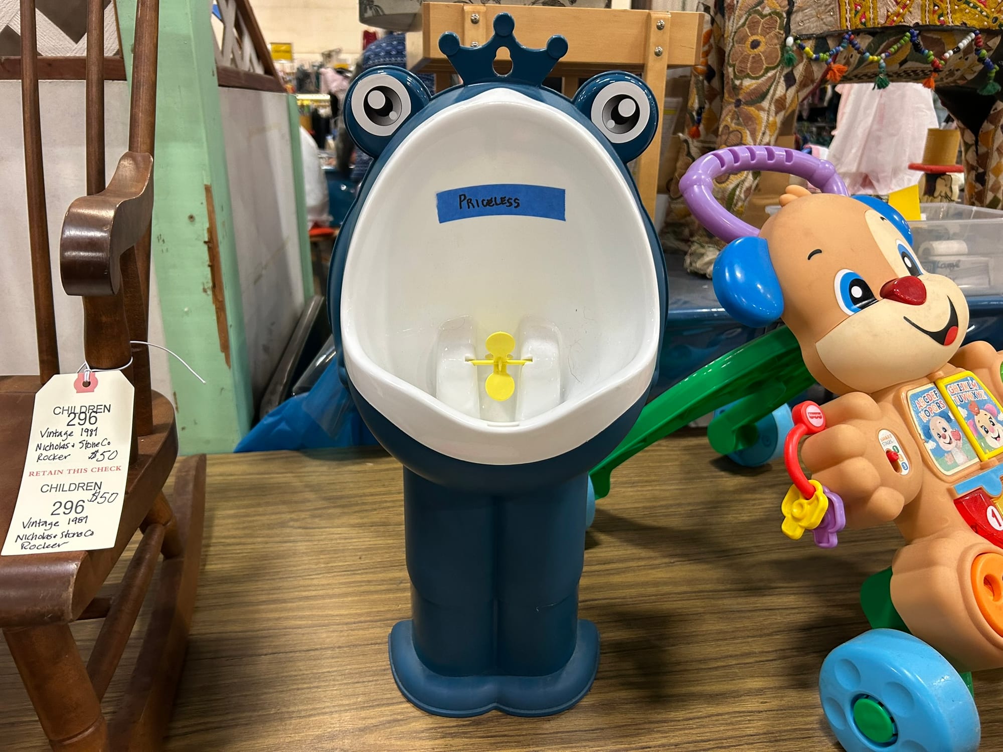 A two-foot-tall blue plastic frog sits on a table with its mouth wide open. Inside is a yellow piece of plastic that spins when it's peed on.