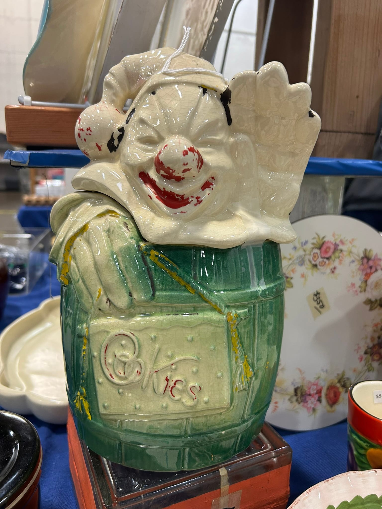 A faded ceramic clown wears a sleeping cap and sits in a green barrel, which says "cookies" along the side.