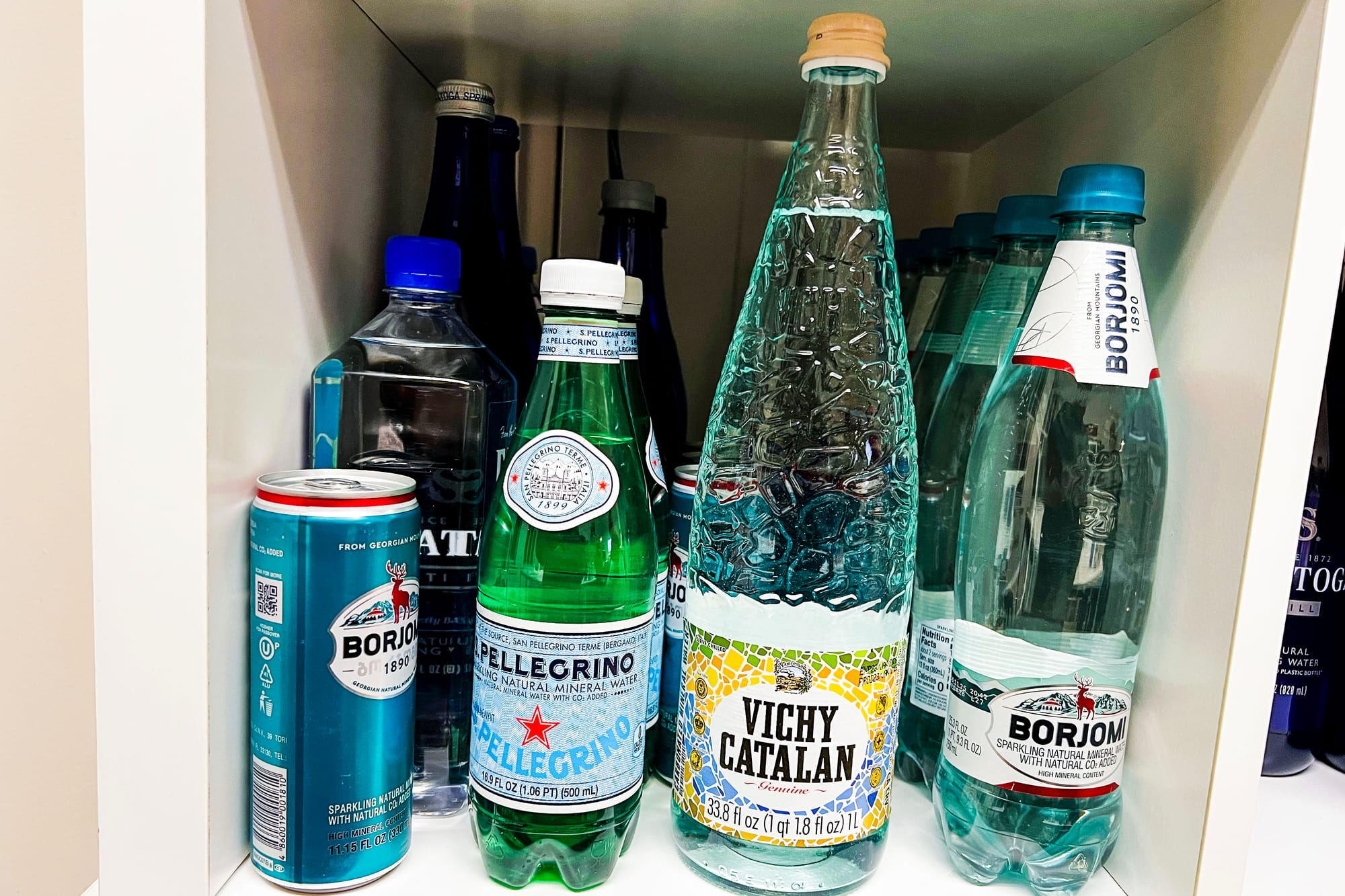 a shelf with different branded water bottles on it, including Pellegrino, Vichy Catalan, and Borjomi