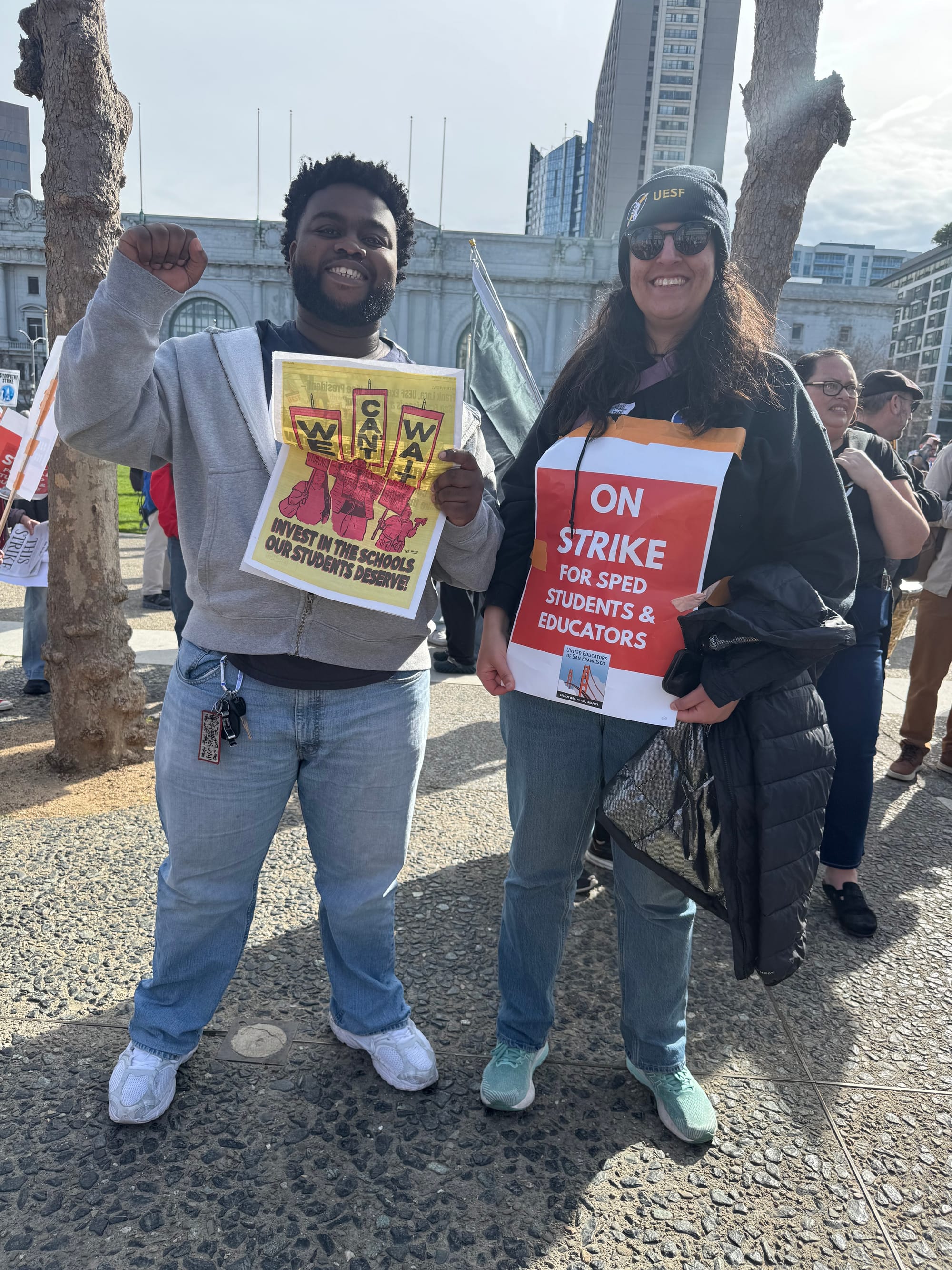 two people hold signs that read 'we can't wait - invest in the schools our students deserve and 'on strike for sped students and educators'