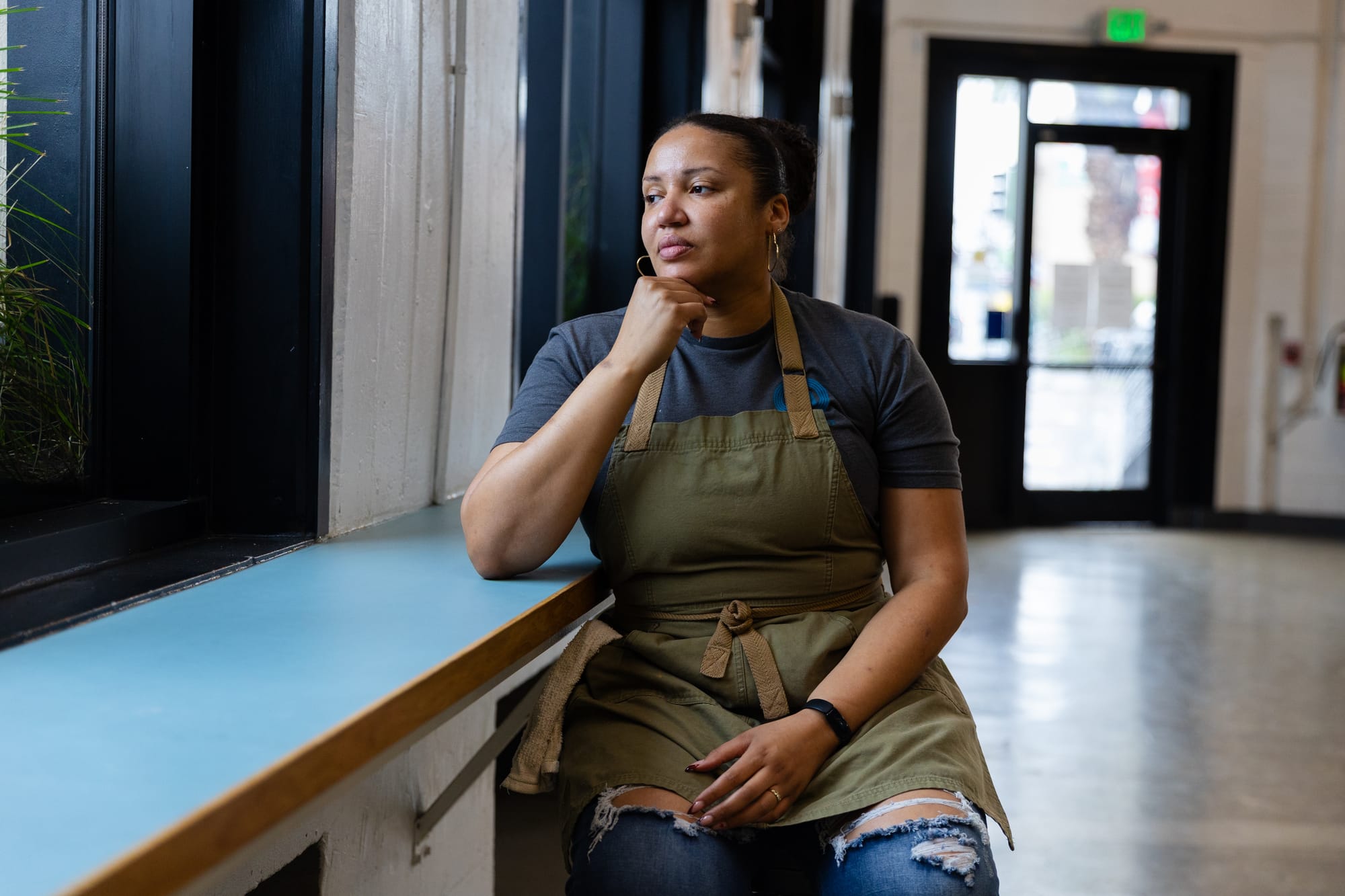 A woman in a chef's apron sits at a counter in an empty cafe.