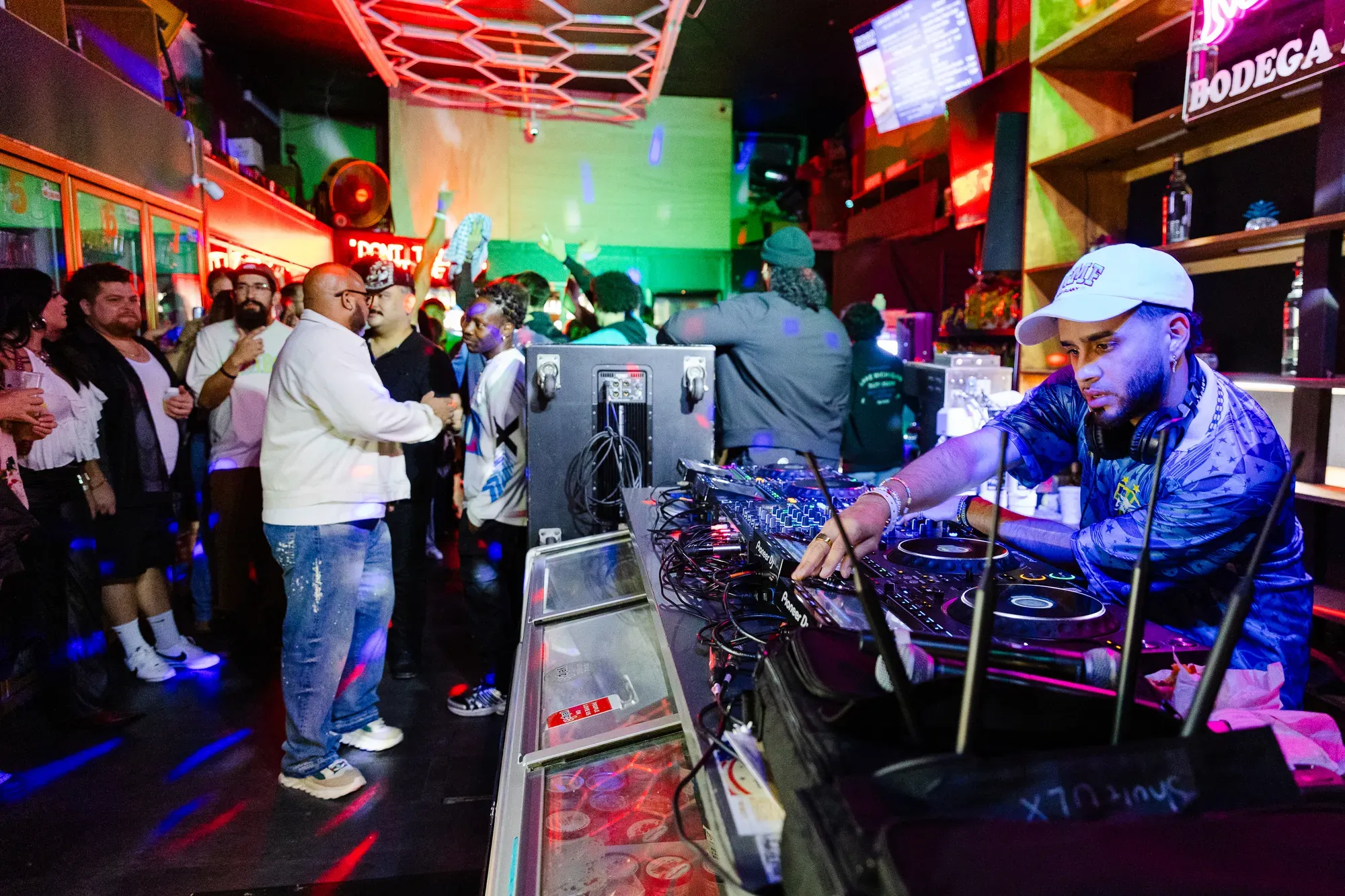 A DJ performs in a liquor store with people dancing in the background. 