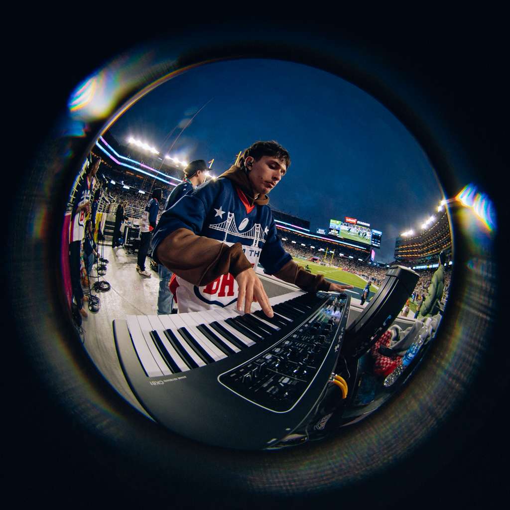 A fish-eye photograph of ClayDough playing the keyboard with a stadium in the background