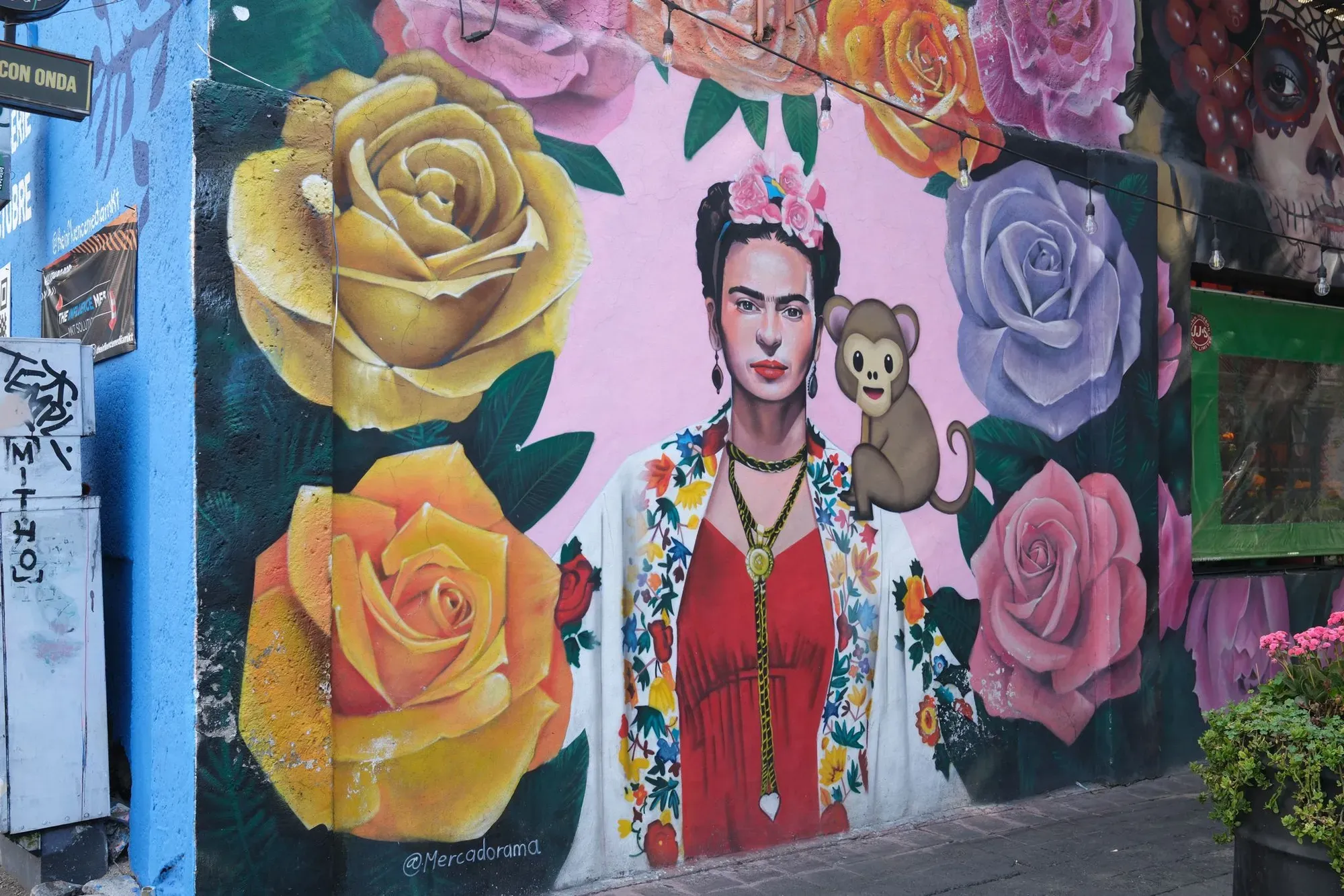A mural features Frida Kahlo with a monkey emoji on her shoulder, surrounded by colored roses