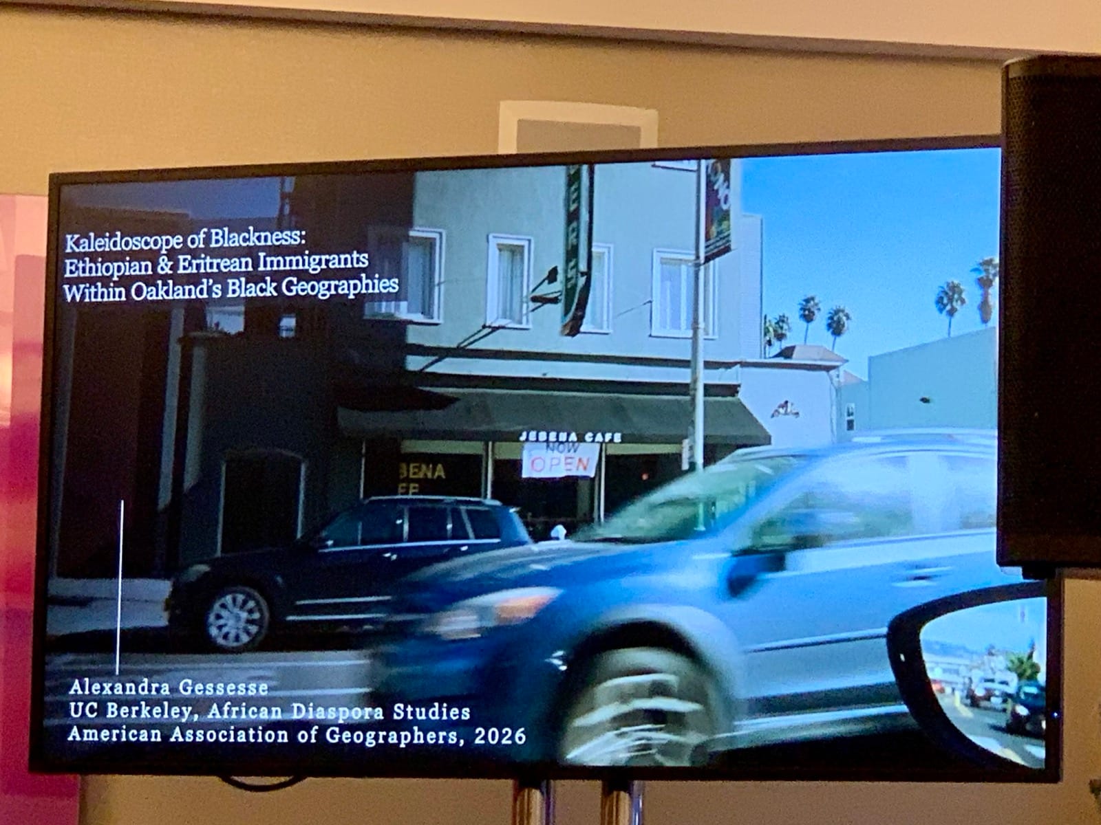 A screen that shows a car driving by and says “Kaleidoscope of Blackness: Ethiopian and Eritrean Immigrants within Oakland's Black Geographies." Below that it says "Alexandra Gessesse UC Berkeley, African Diaspora Studies American Association of Geographers, 2026" 