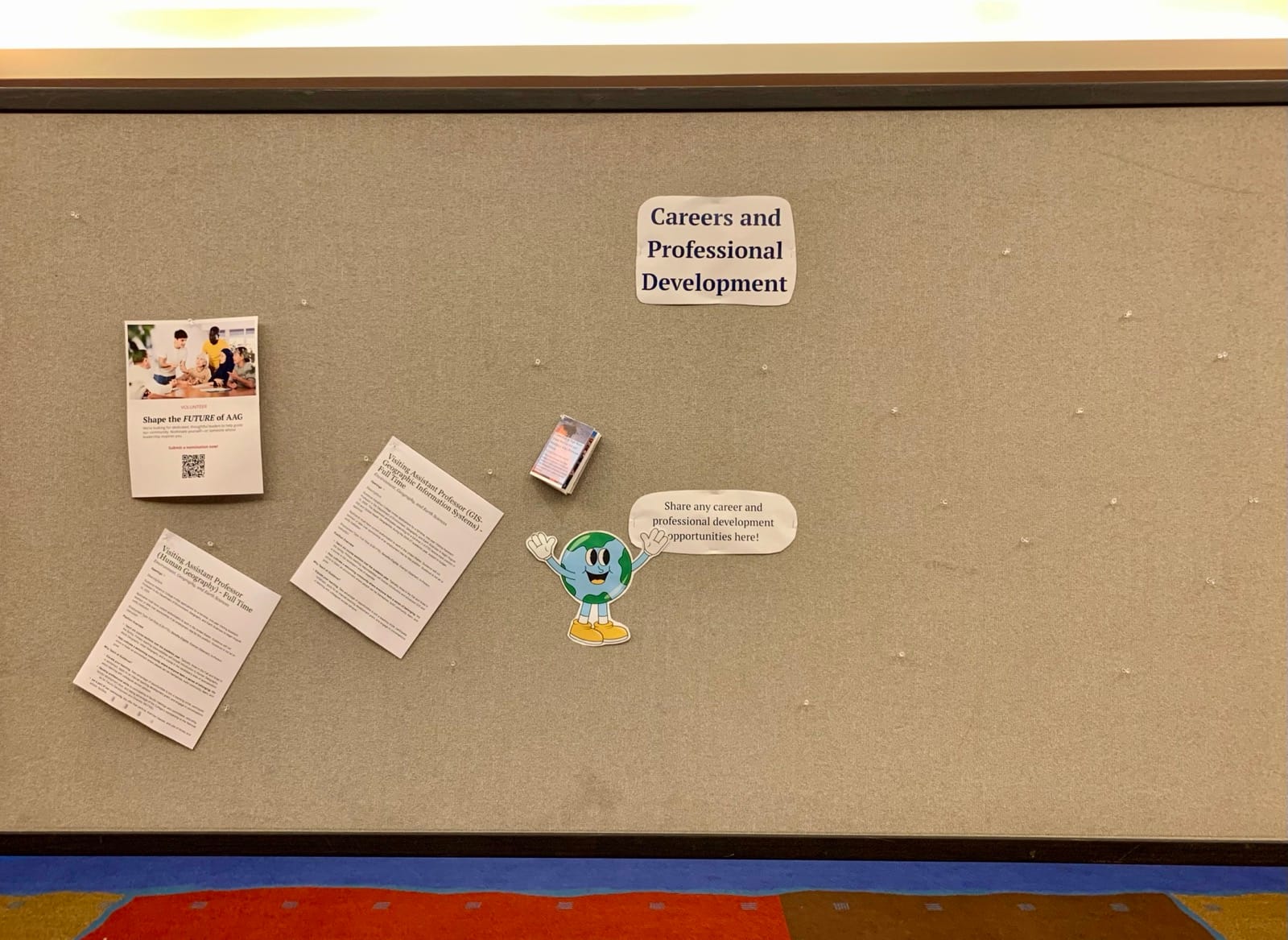 A photo of a mostly empty jobs board. Near the top, a pushpin holds a sign reading “Career and Professional Development” above a cartoon of a smiling globe with its arms open.