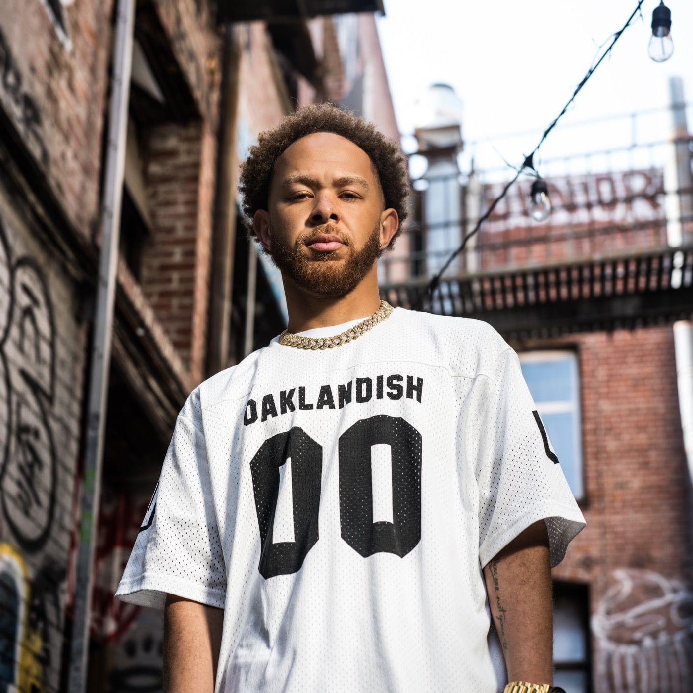 Jwalt is wearing a white jersey with "Oaklandish zero zero" on the front, and a thick gold chain necklace