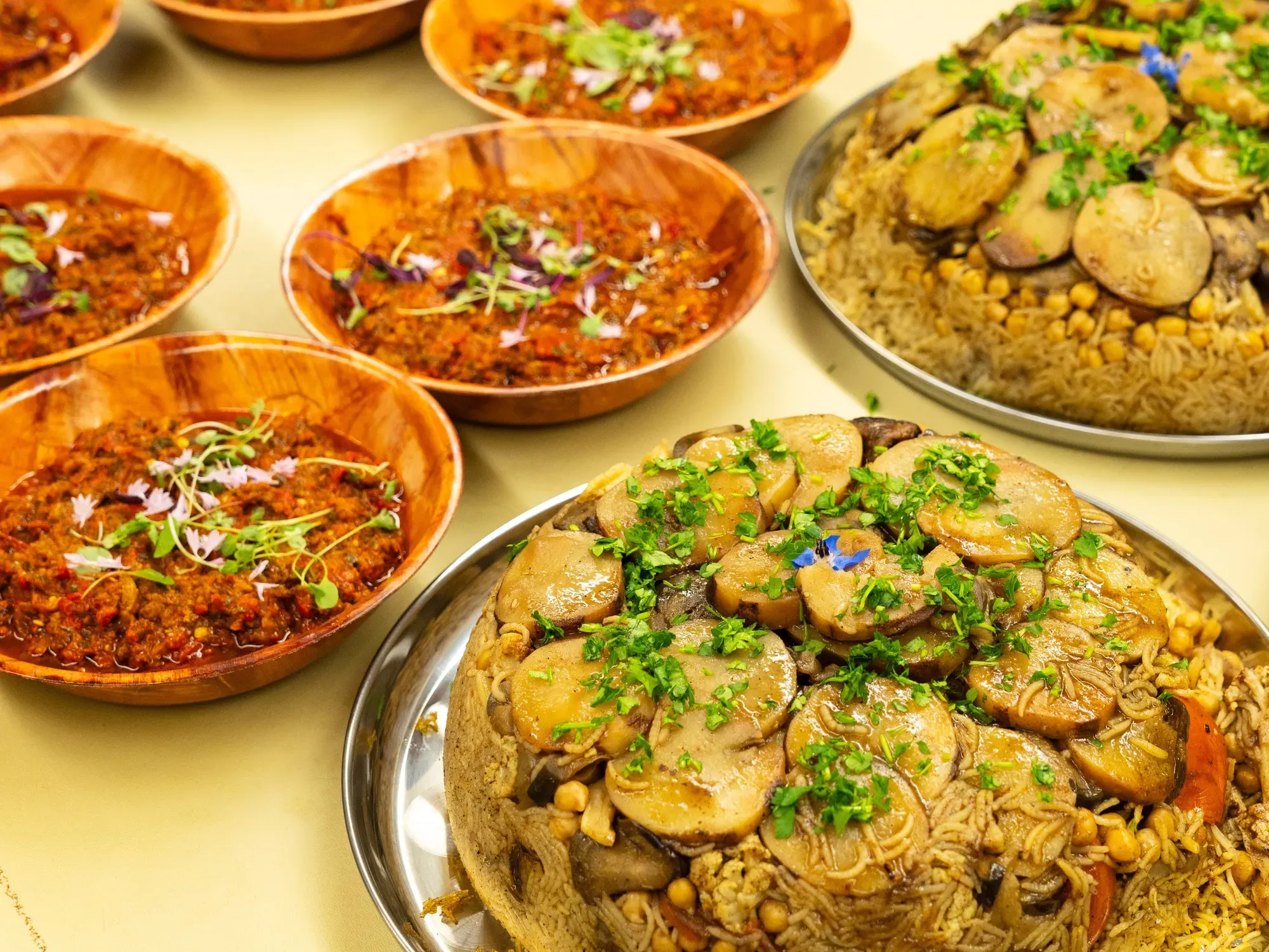 Two platters of vegan maqluba on a table next to four bowls of shakshuka.