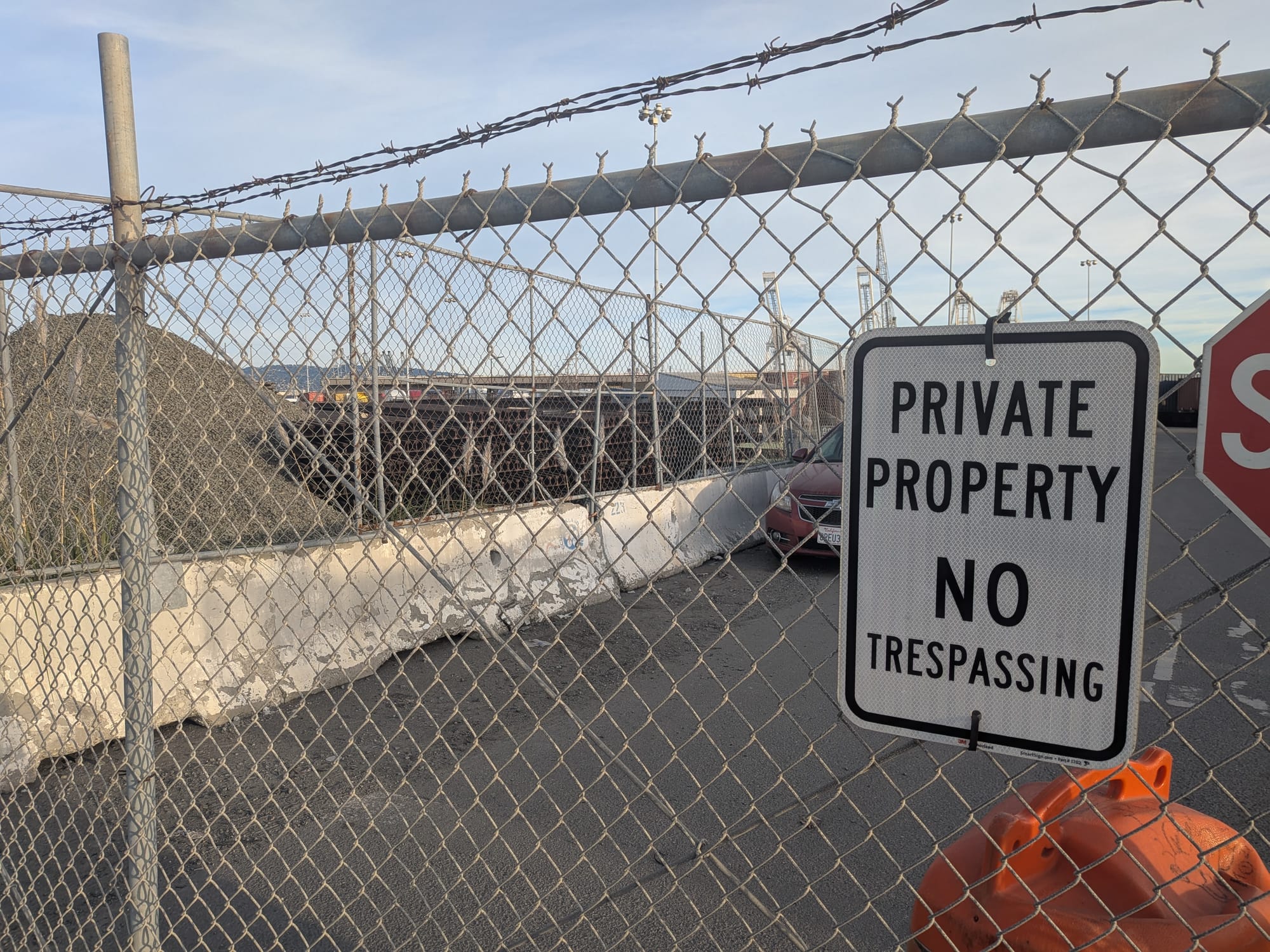 a private property no trespassing sign on a fence in front of a parking lot/pile of gravel