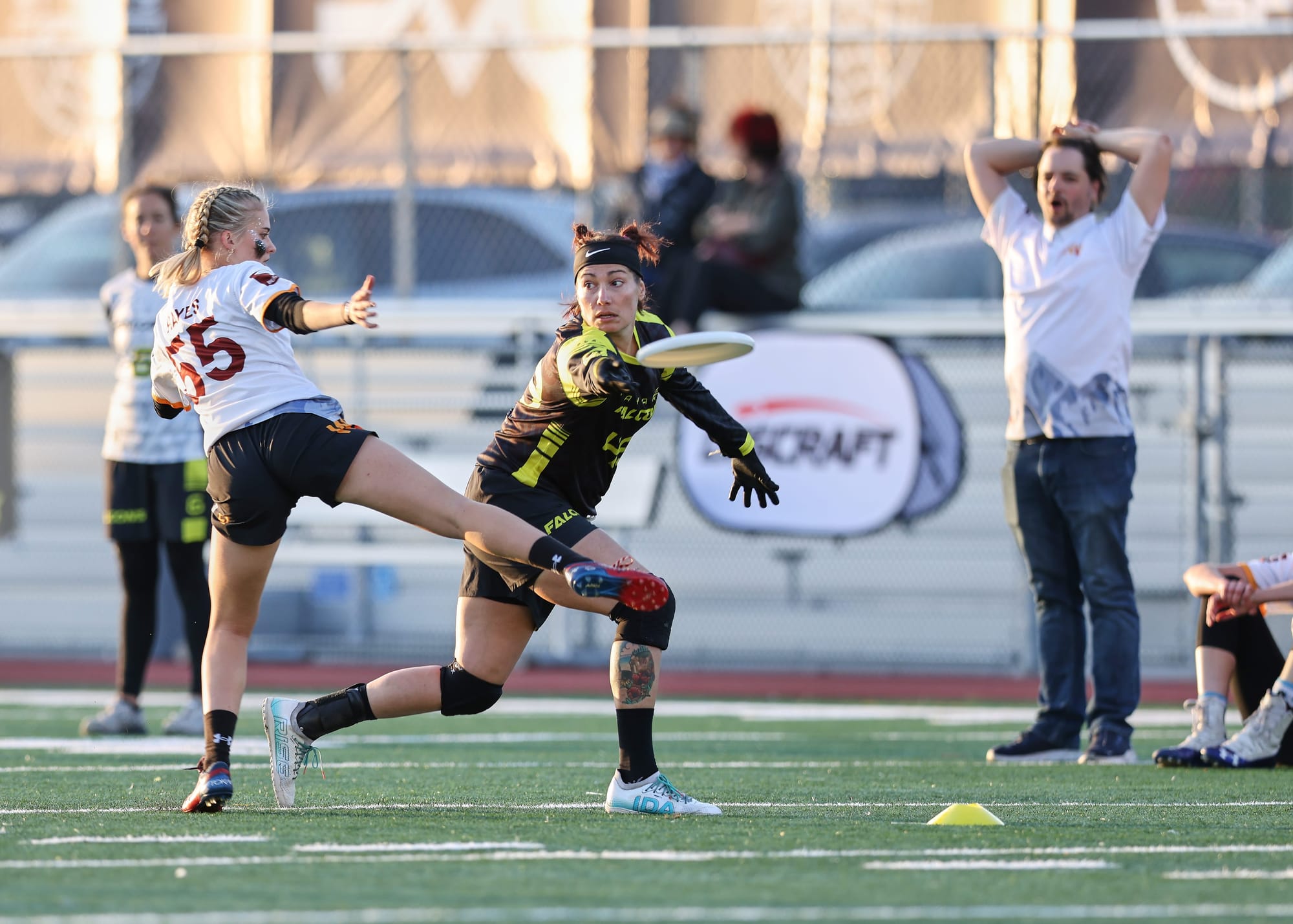 An ultimate frisbee player wearing black and yellow throws a disc around her opponant who is wearing white and red.