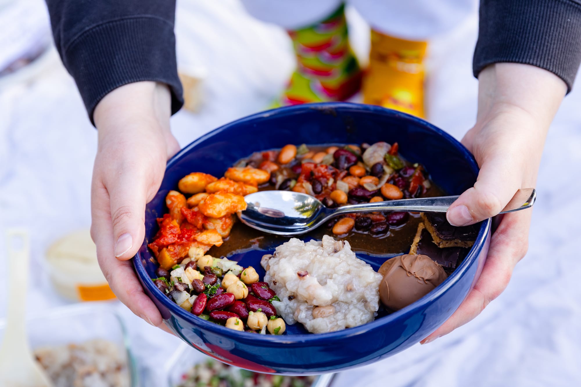 Two hands hold a blue bowl filled with different types of bean dishes