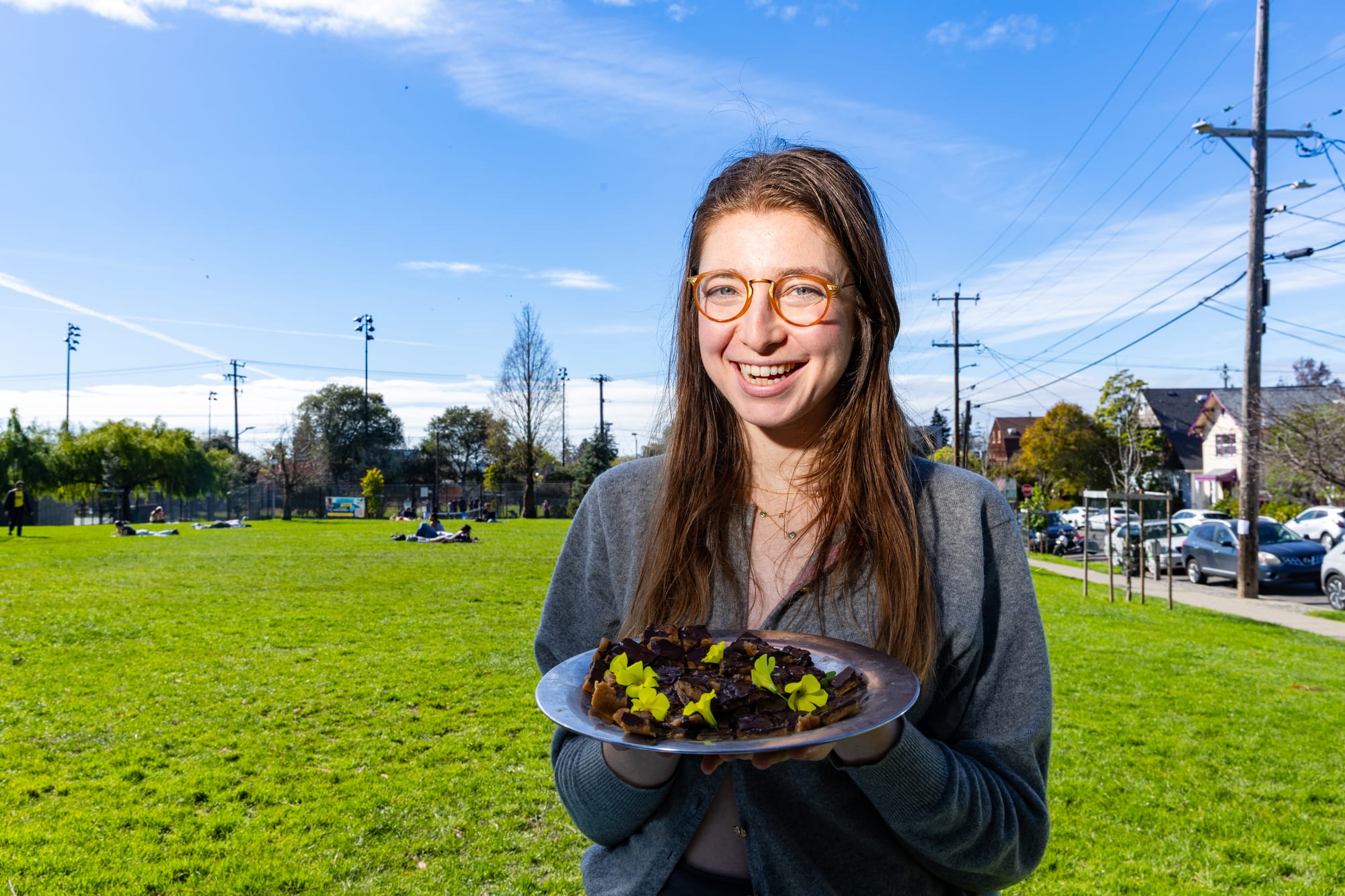 A woman with brown hair and orange classes holds a plate filled with food in a park