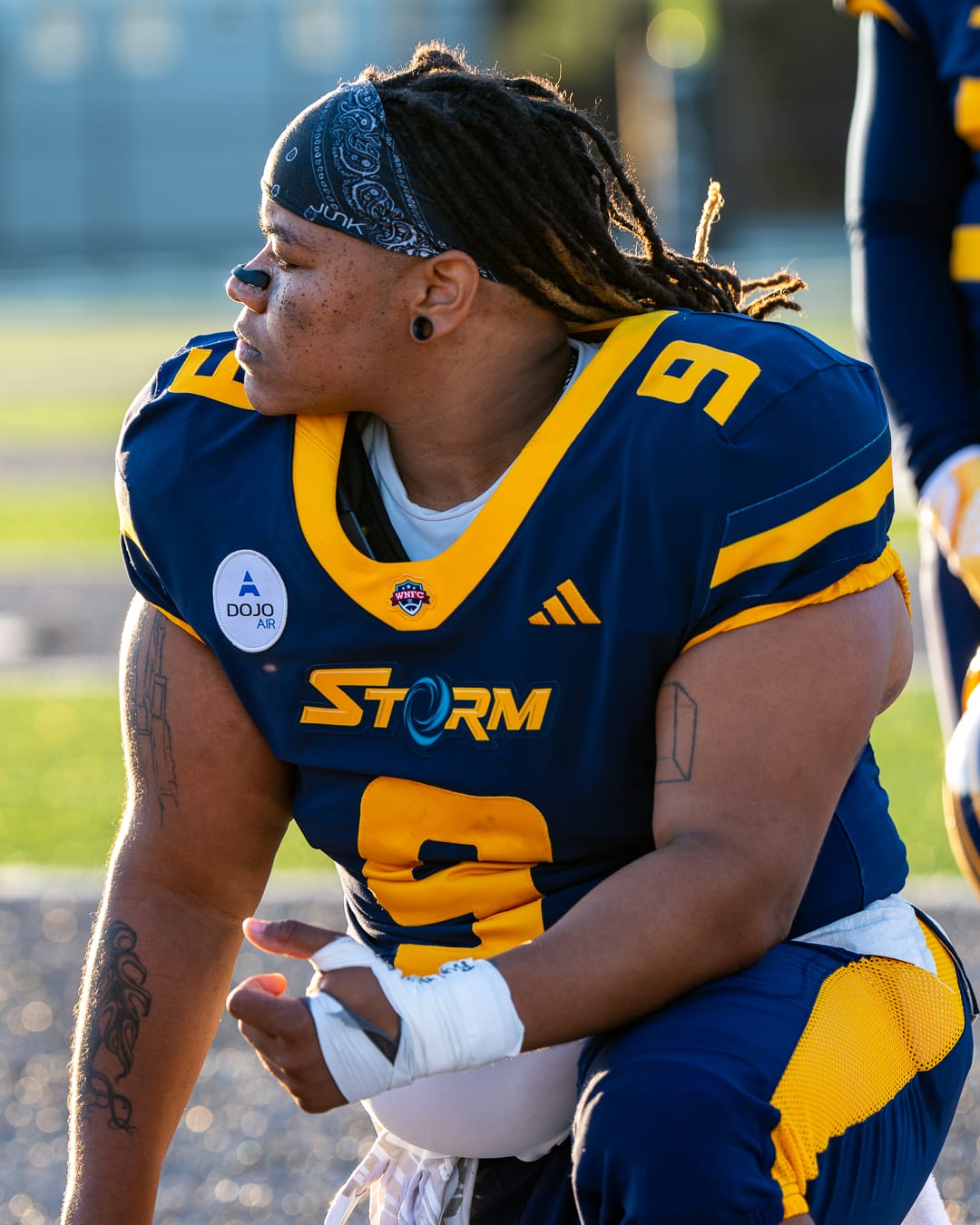 A player with dreadlocks and a black bandana takes a knee and looks off to the left of the camera.