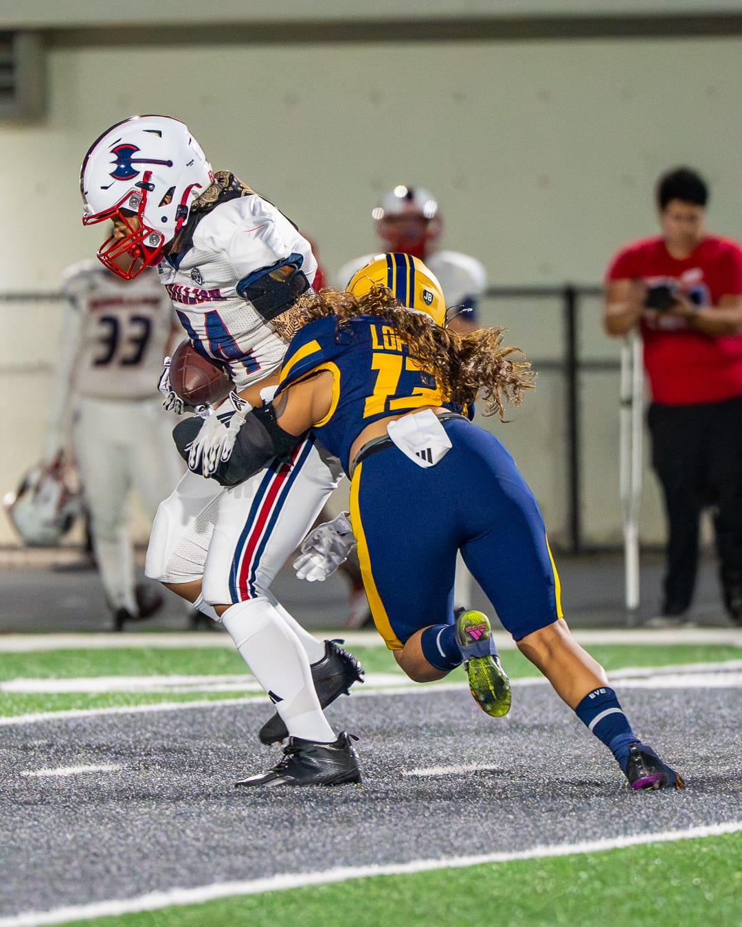 A linebacker in a blue uniform tackles a player with the ball wearing a white uniform.