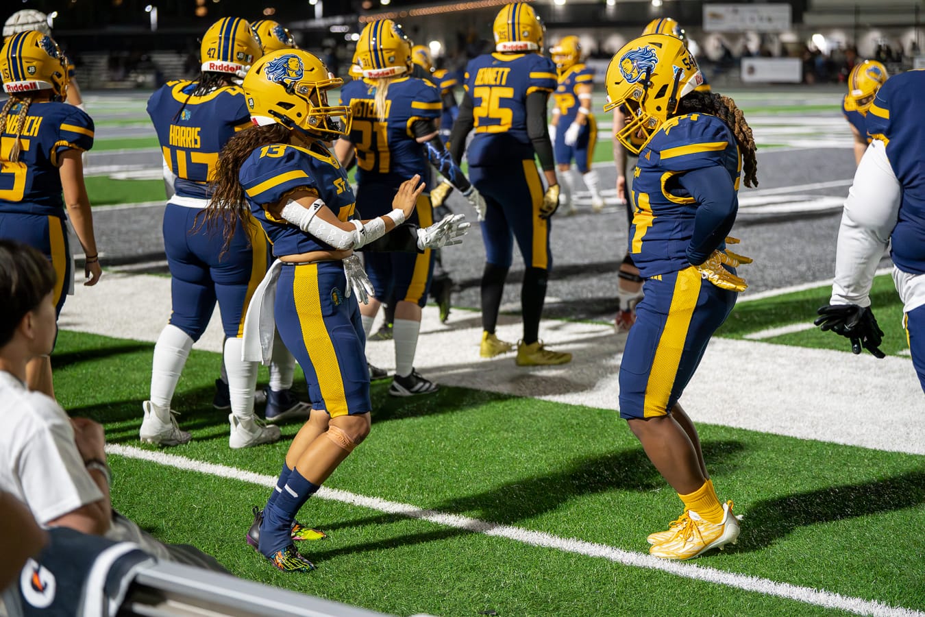 Two football players in blue uniforms dance on the sidelines.