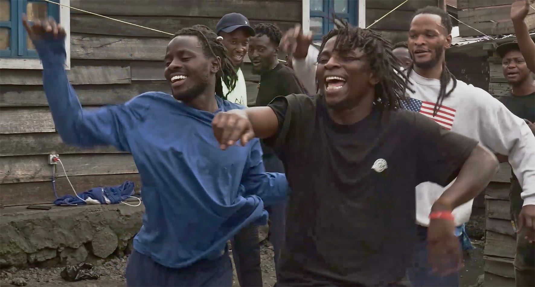 a group of 7 Black men outside an old wooden structure, they look like they're having a good time