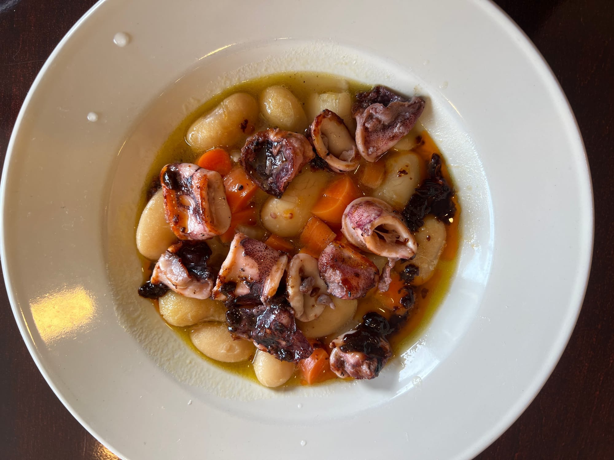 Sliced squid served on top of white beans in a white bowl.