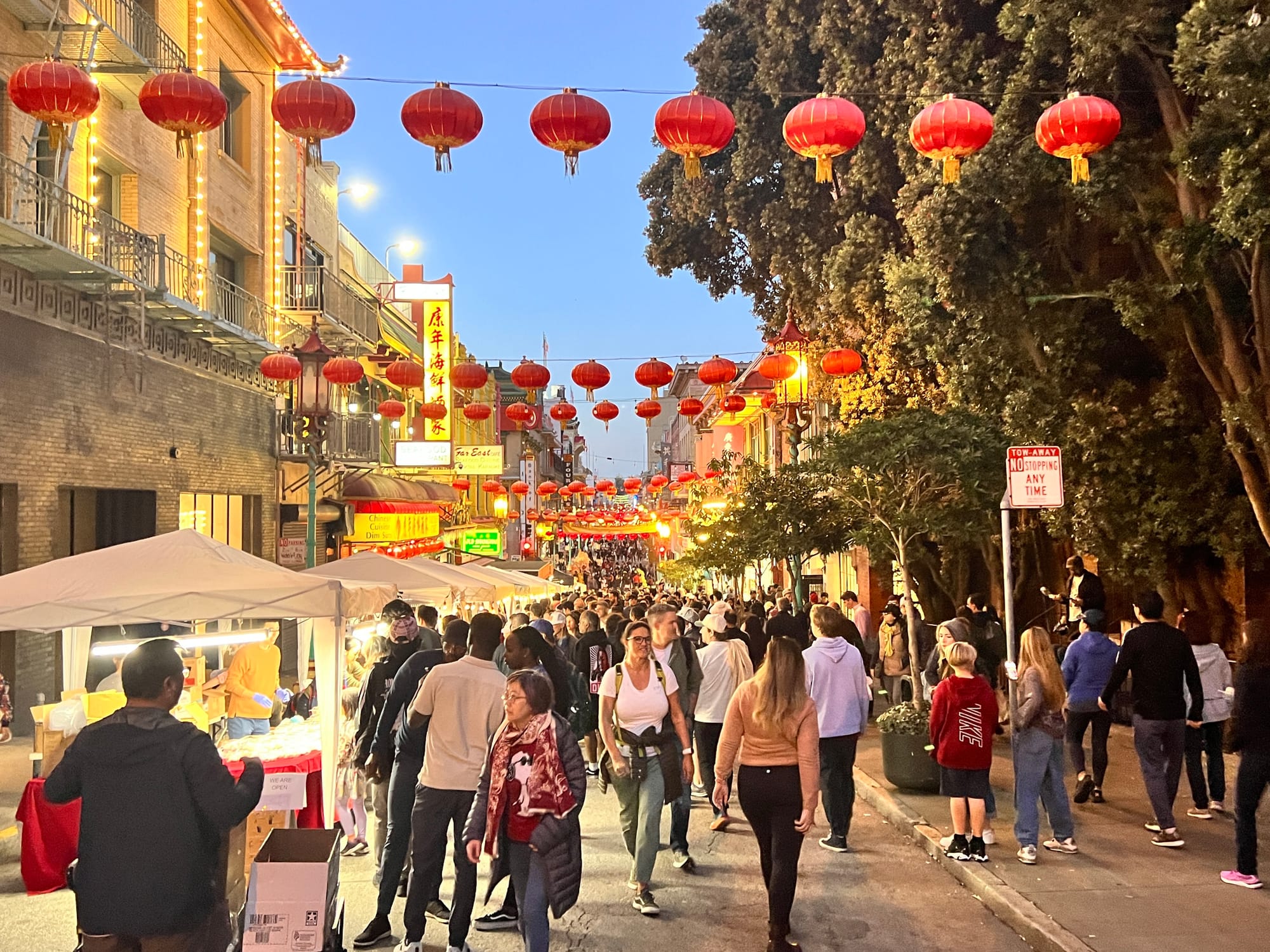 people walk down a street in chinatown with red lanterns overhead