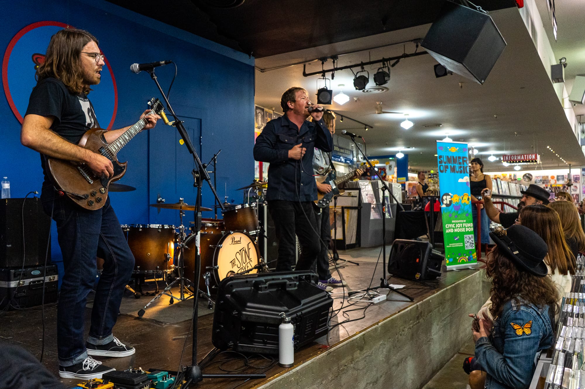 a band performs on a stage in a record store against a blue wall