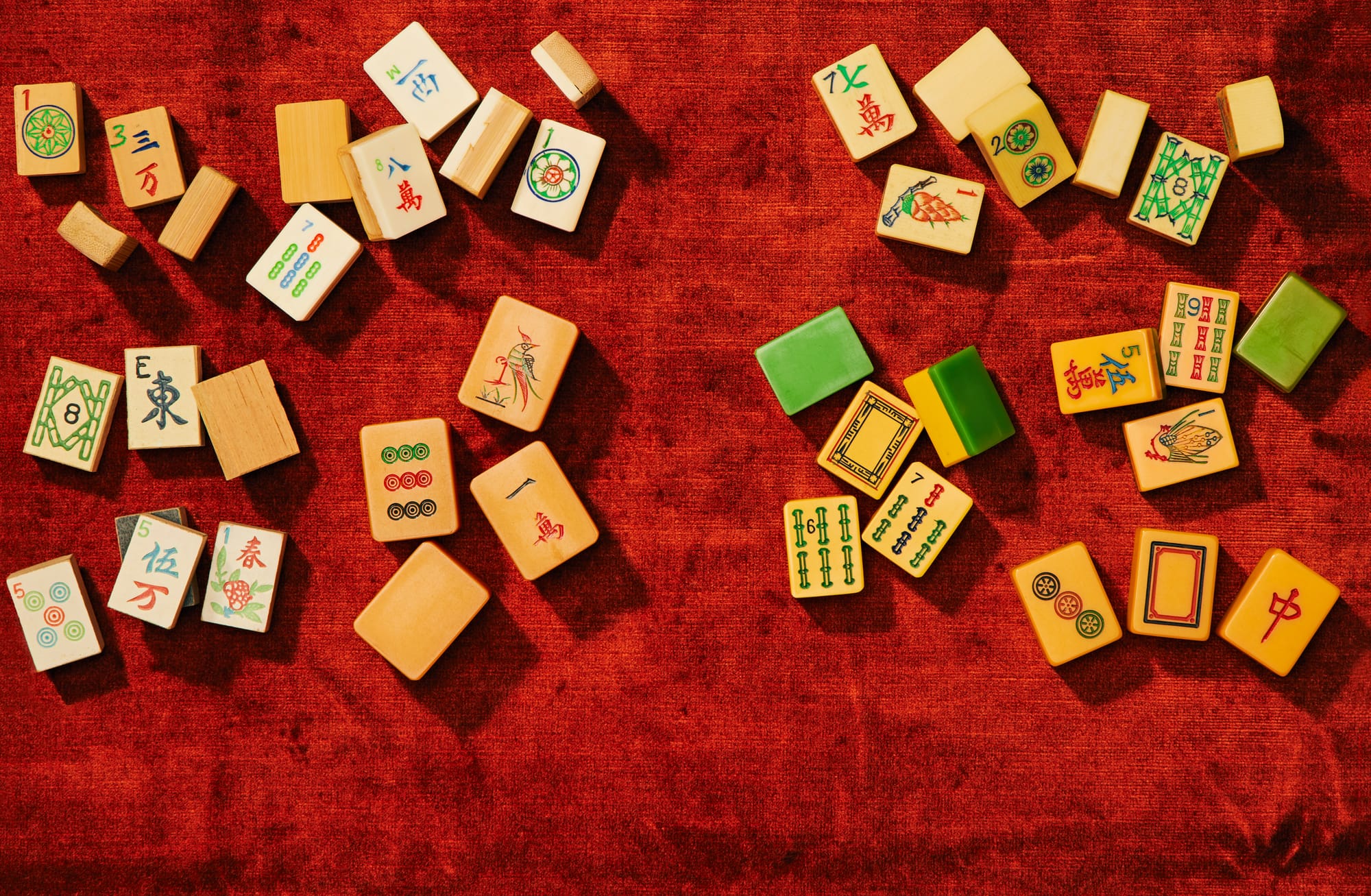 Various mahjong tiles scattered on top of a red velvet-covered tabletop.