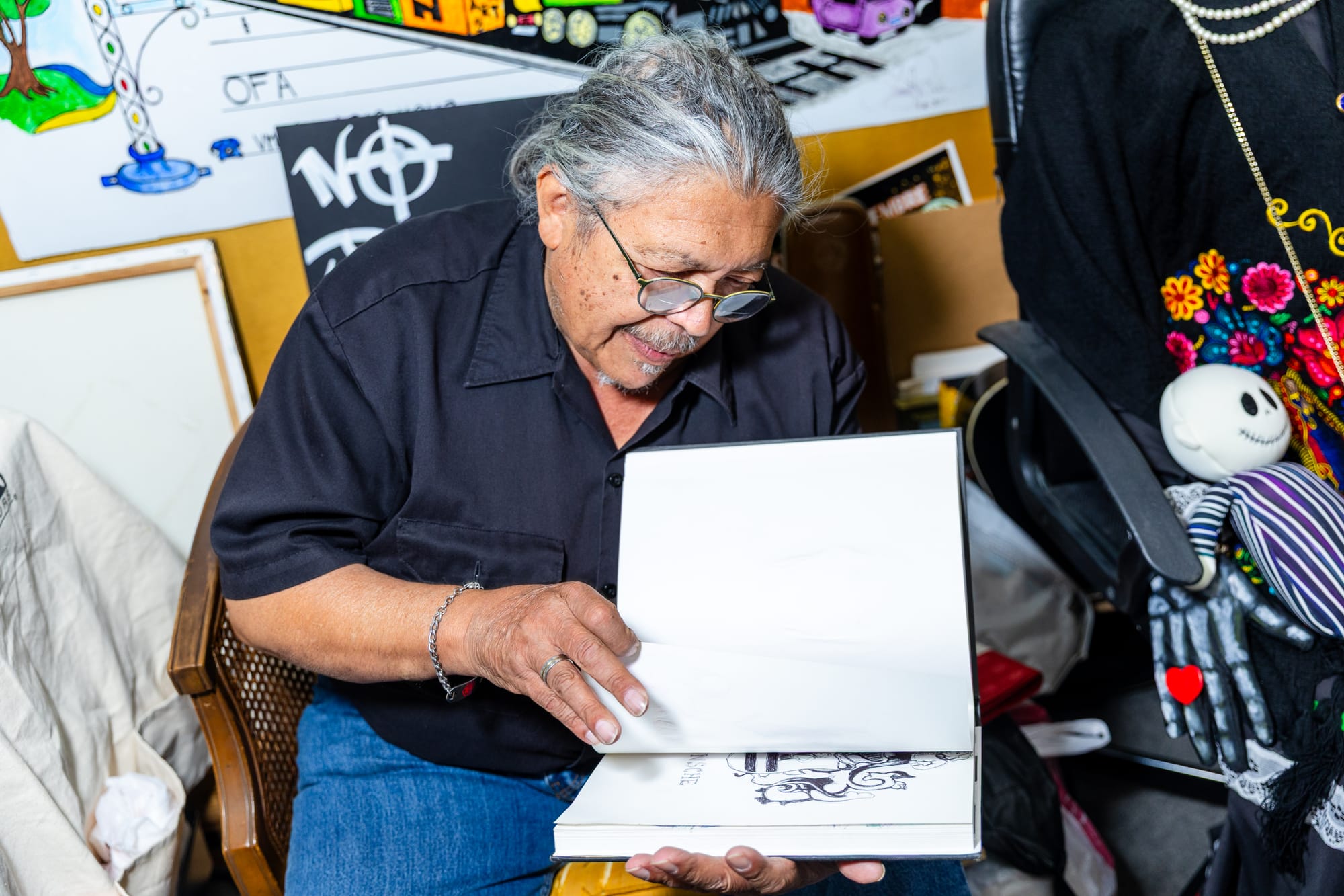 A man sits in a chair, and flips through a notebook full of sketches.