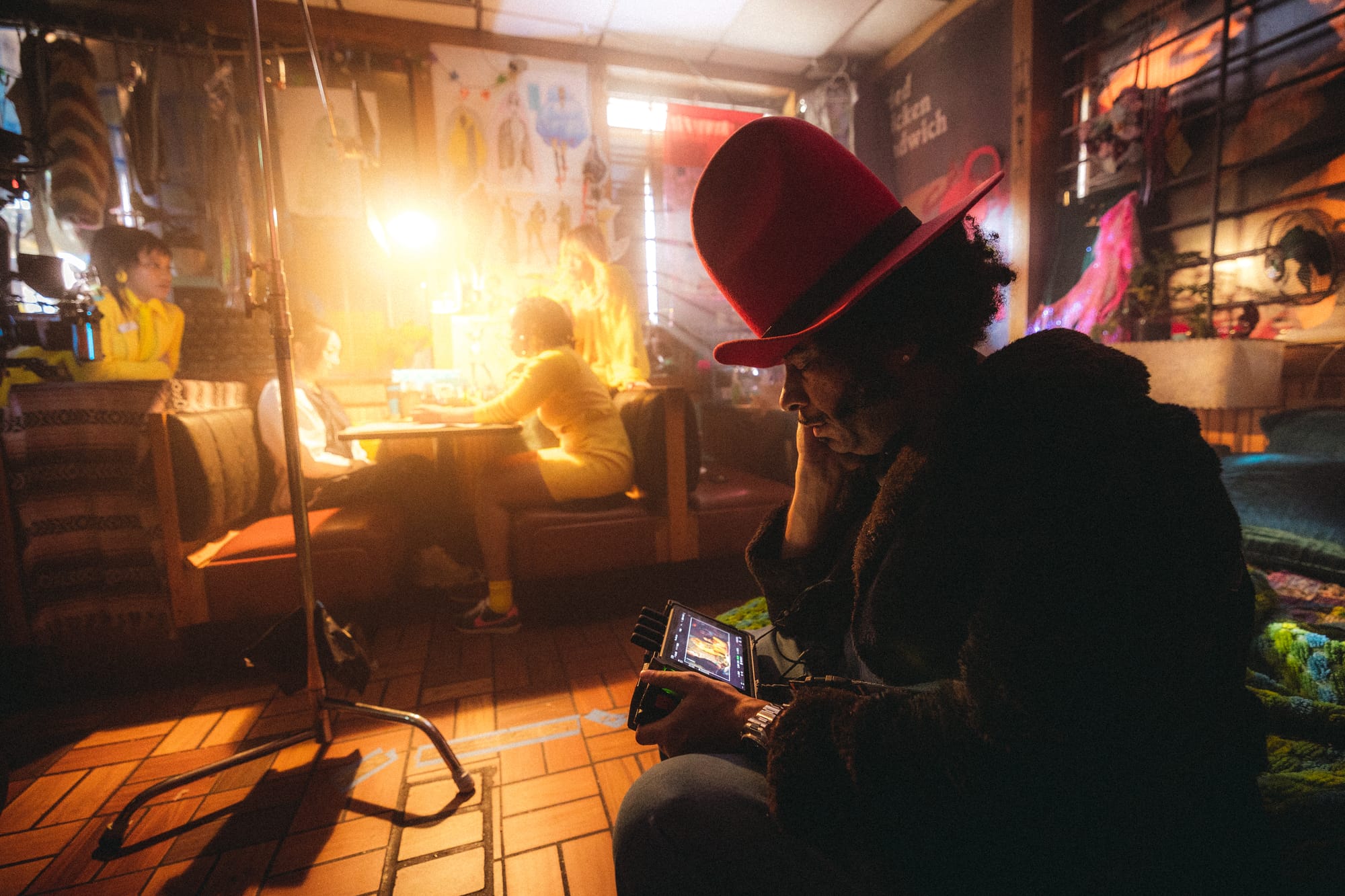 a film still of a man in a tall hat looking at a camera screen on a film shoot