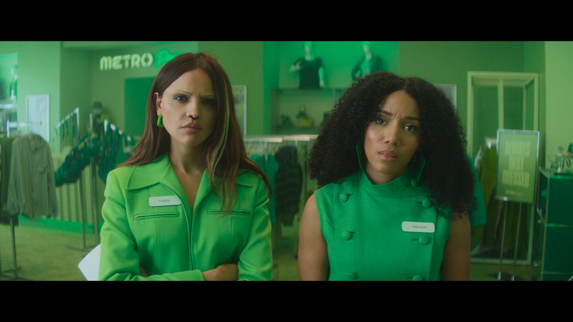two women dressed all in green look into the camera in a film still