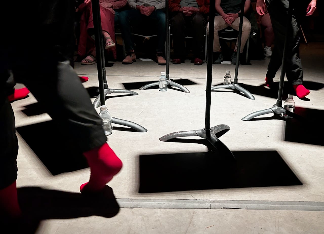 people's feet in red socks and black pants walk around a stage with the shadows of music stands