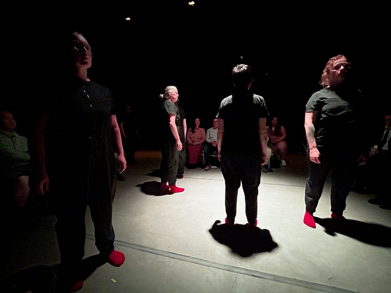 four people dressed in black with red socks on stage in front of an audience