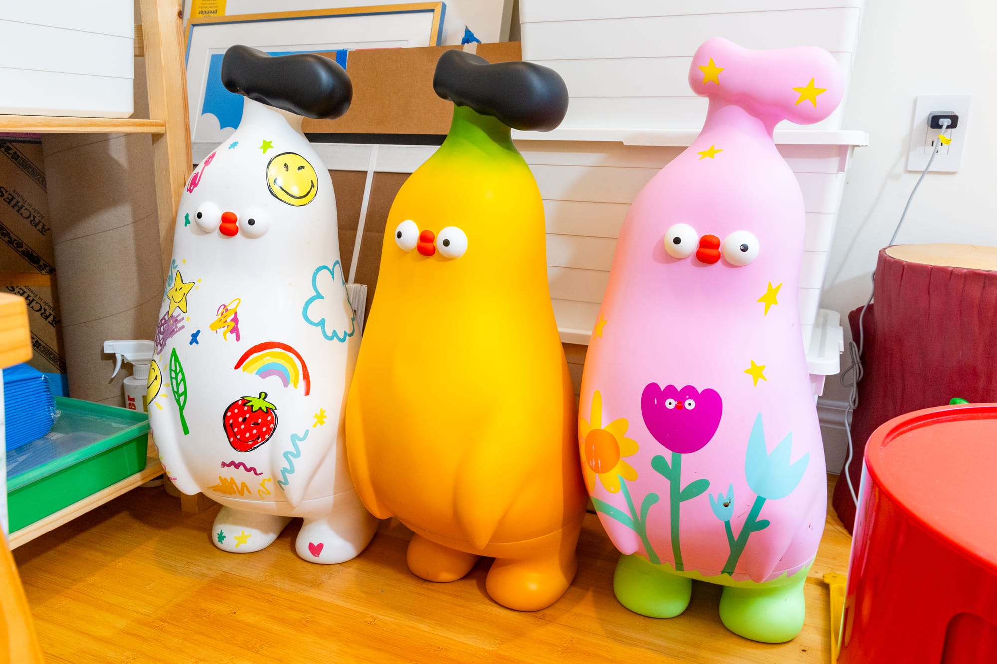 Three banana-shaped statues that are about 4 feet tall and painted with rainbows, clouds, and flowers.