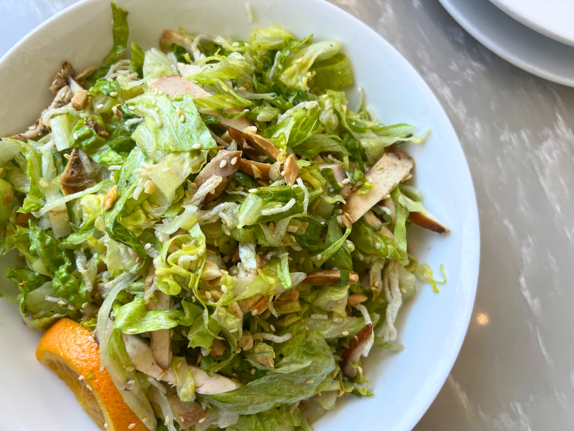 Close shot of a salad of shredded lettuce, thinly sliced chicken, sesame seeds, and fried rice noodles.