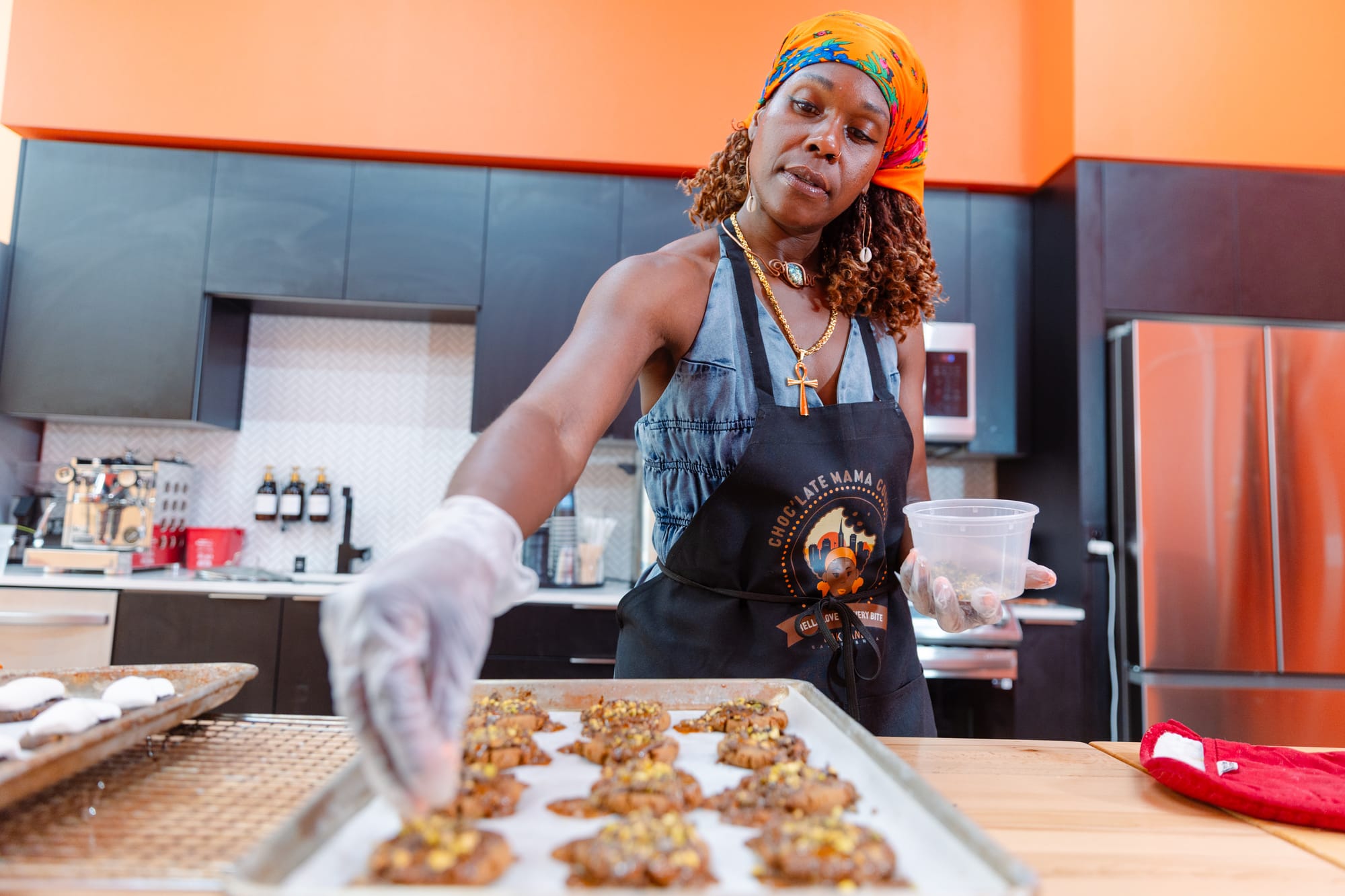 Woman in an orange kerchief on her head decorating unbaked cookies with chopped nuts.