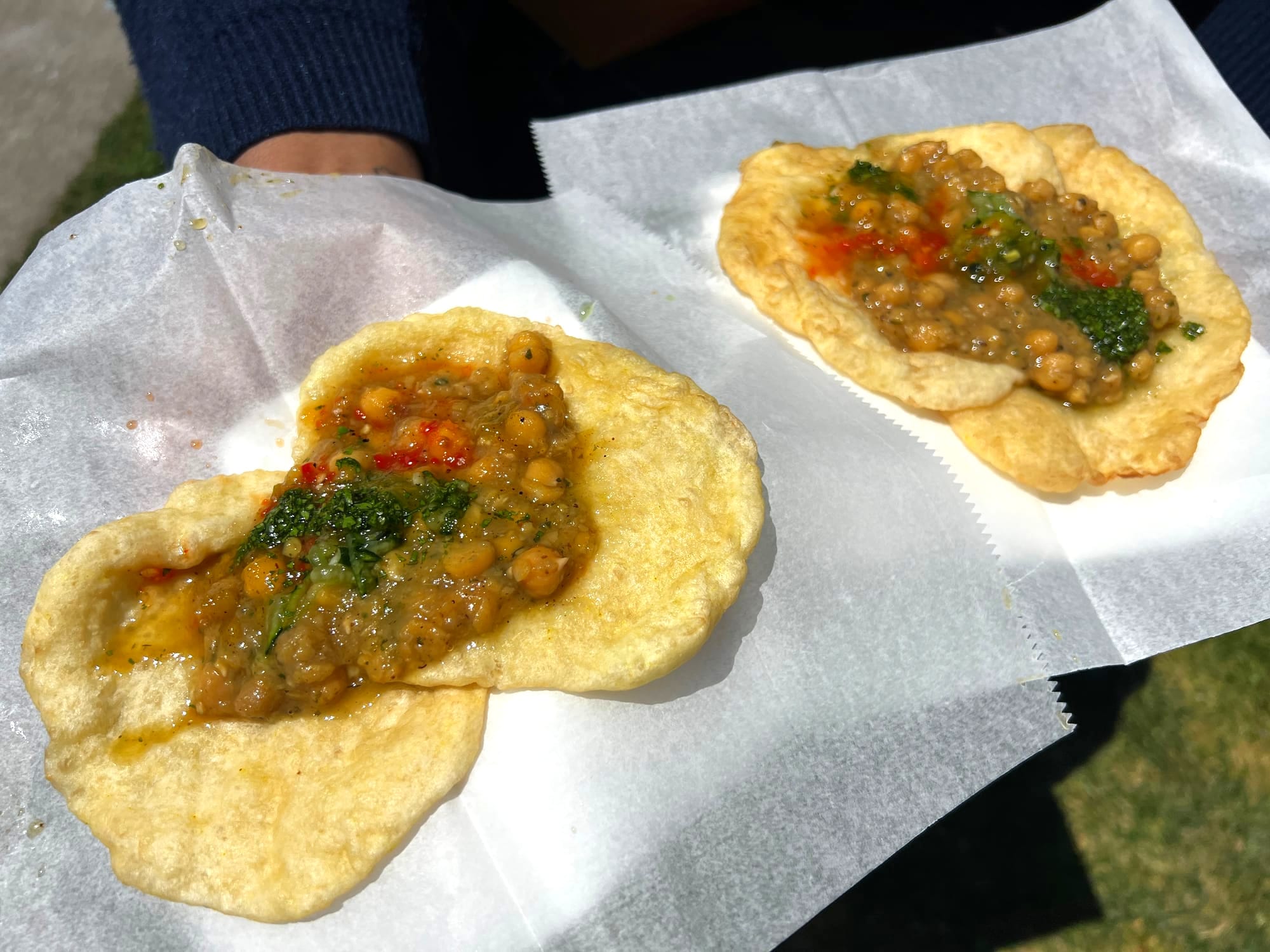 Person holding two orders of Trini doubles, each with chickpeas and red and green sauces on top.