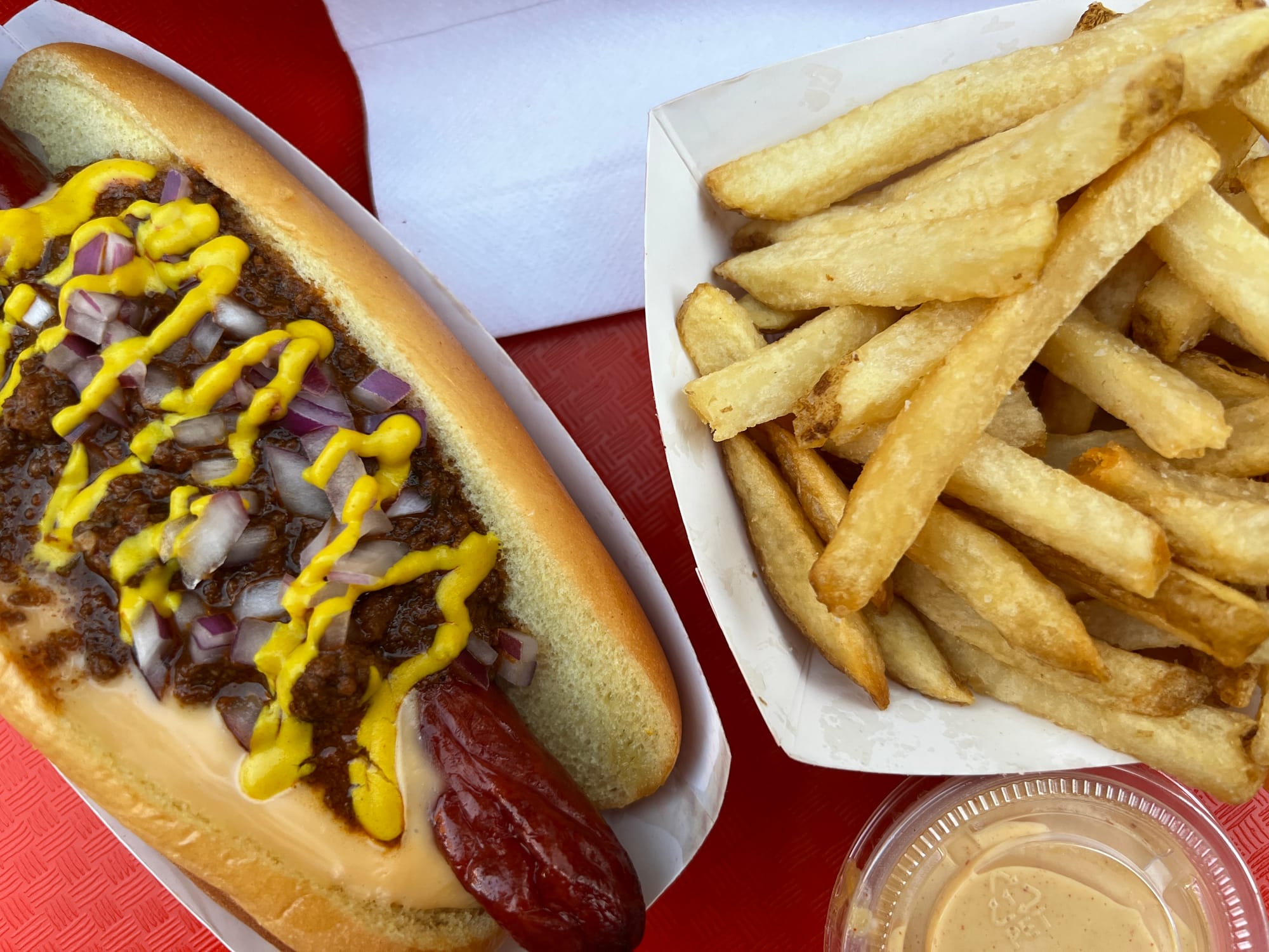 Close shot of a chili cheese dog on a red tray with fries.