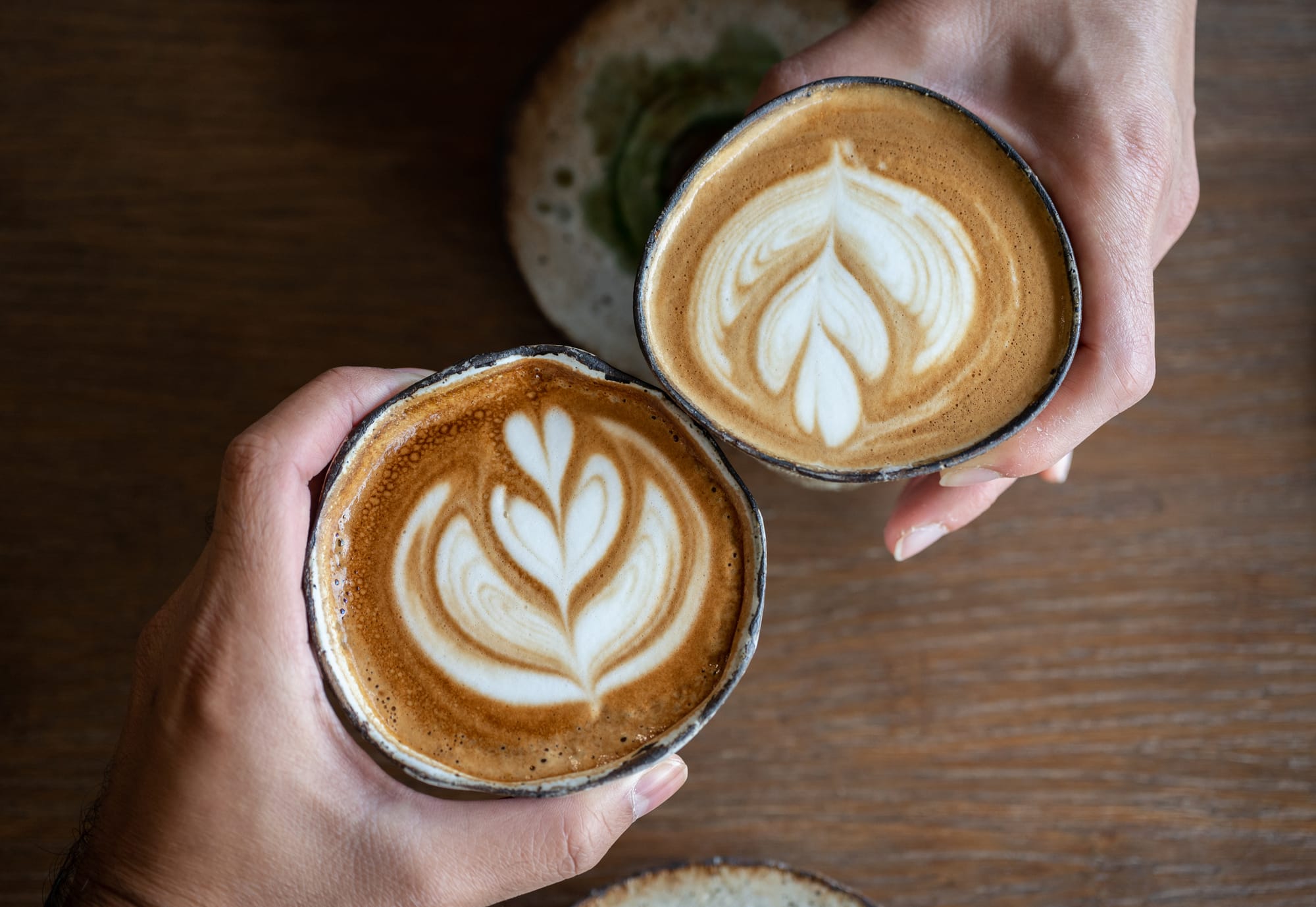 Two hands holding cups with leafy latte art