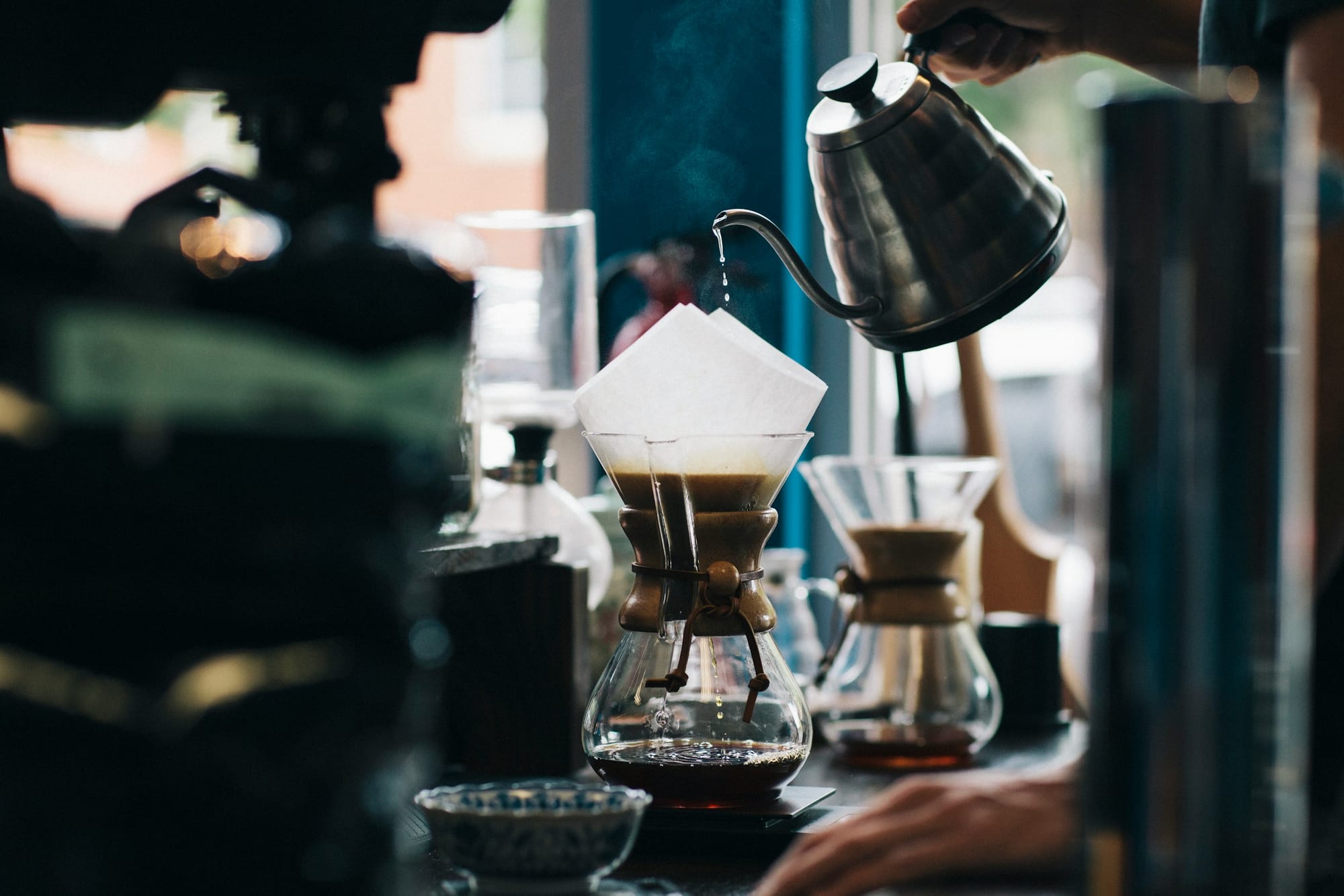 A person pouring hot water over a paper filter fitted on a Chemex.