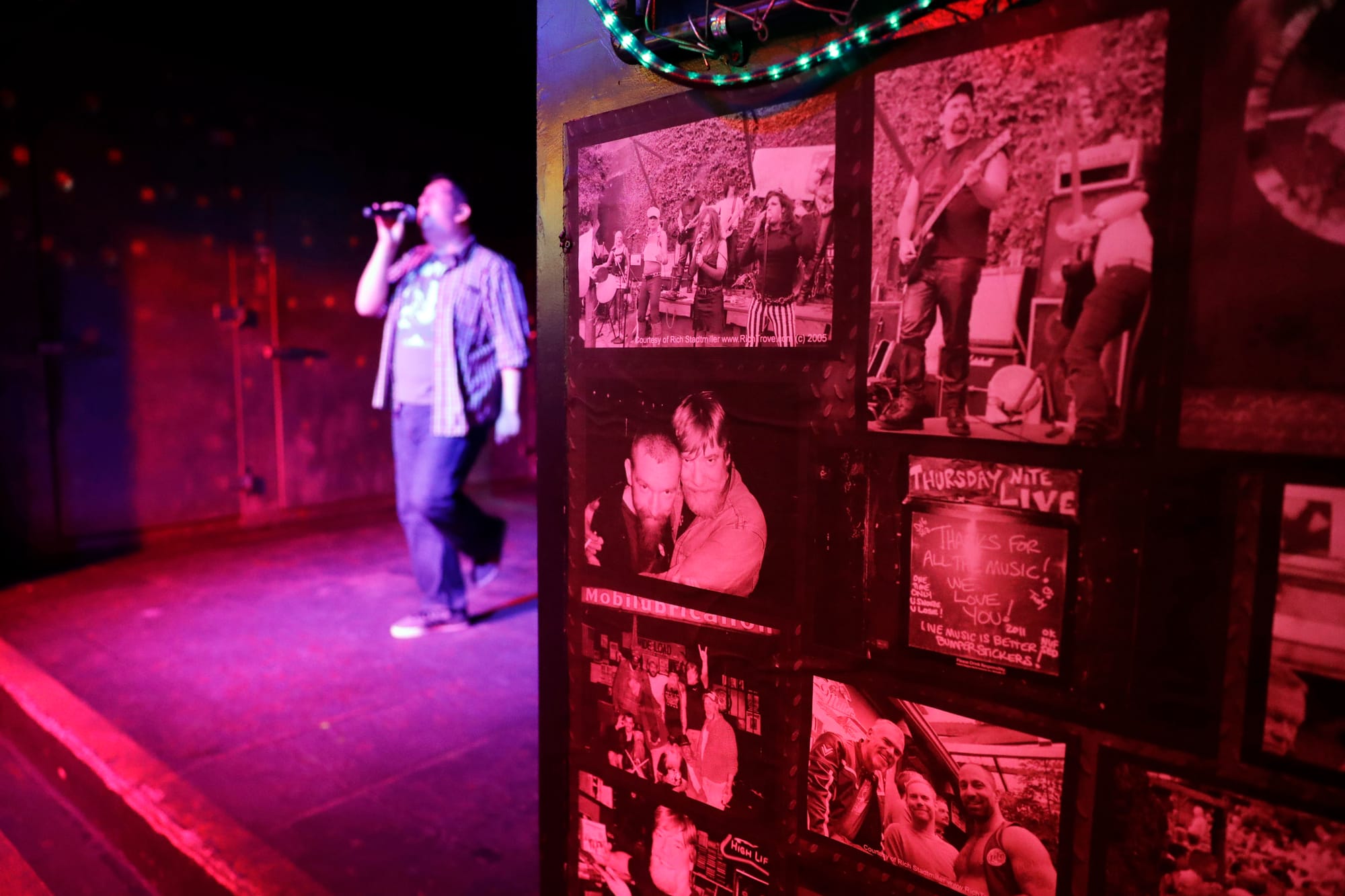a person does karaoke in a red-lit bar with photos on the wall