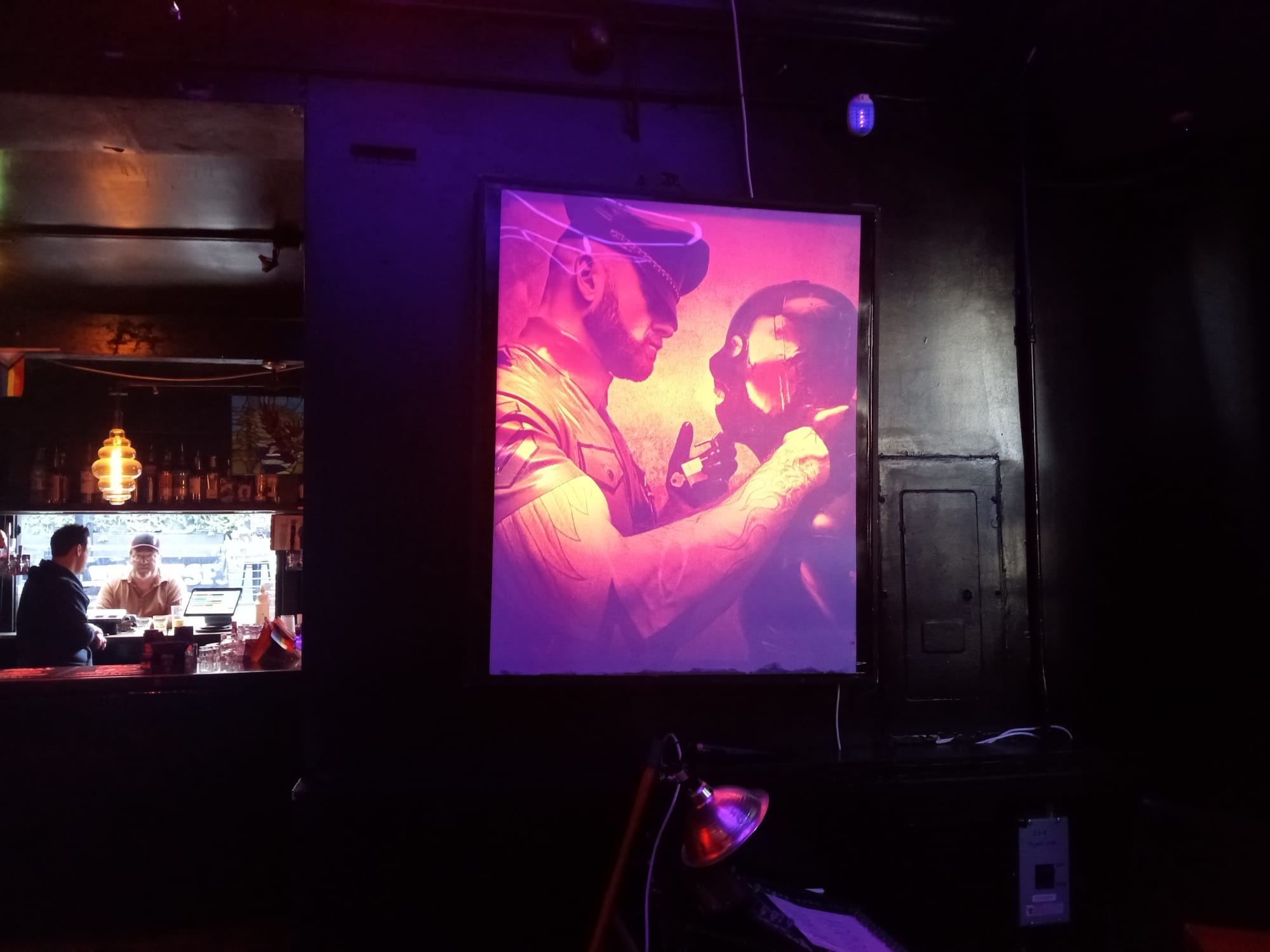 the interior of a bar with a large backlit sign of two men in leather play