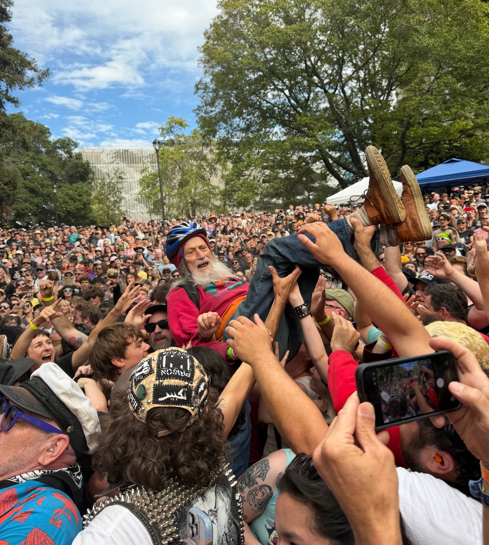 a man in his 70s wearing a bike helmet crowdsurfs at a crowded outdoor music festival