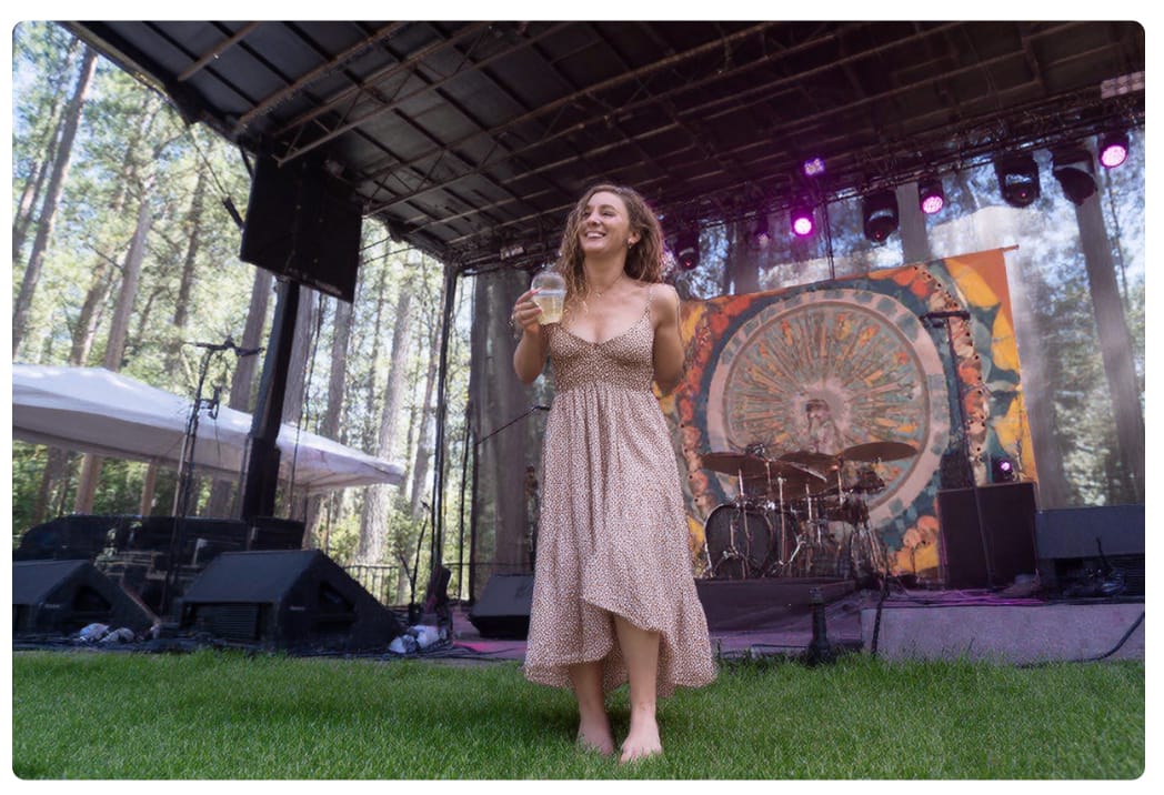 an AI-generated woman missing an arm standing in grass in front of a stage