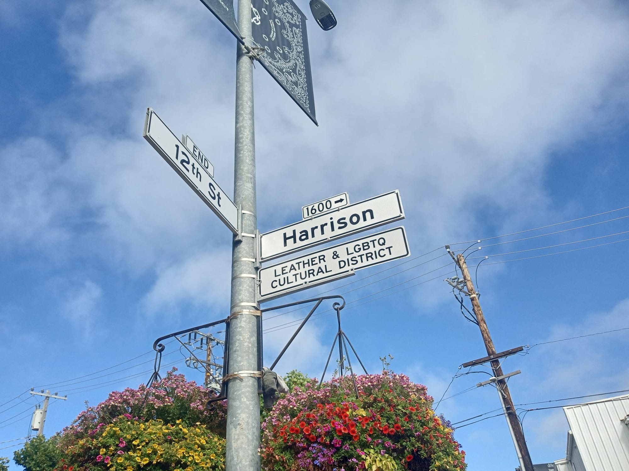a street sign showing the intersection of 12th and Harrison Streets in San Francisco, with a sign denoting "leather & LGBTQ cultural district" against a blue sky 