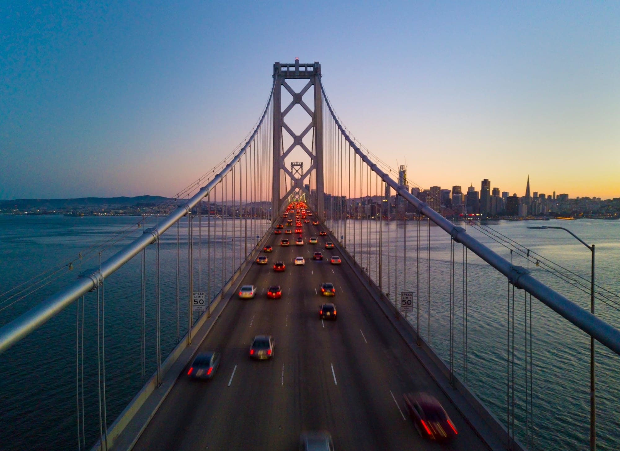 Cars with their tail lights on on the bay bridge to San Francisco during sunset