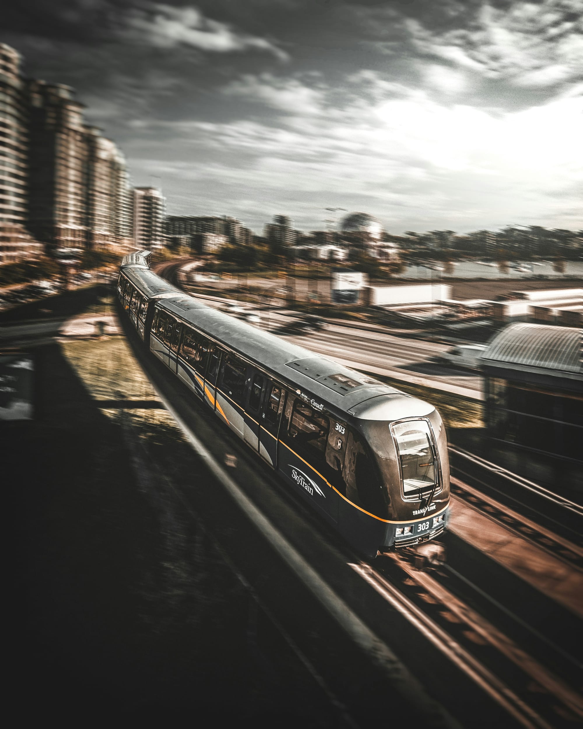 a sleek bullet train in Vancouver runs on the tracks with a dramatic cloudy sky and skyline in the background
