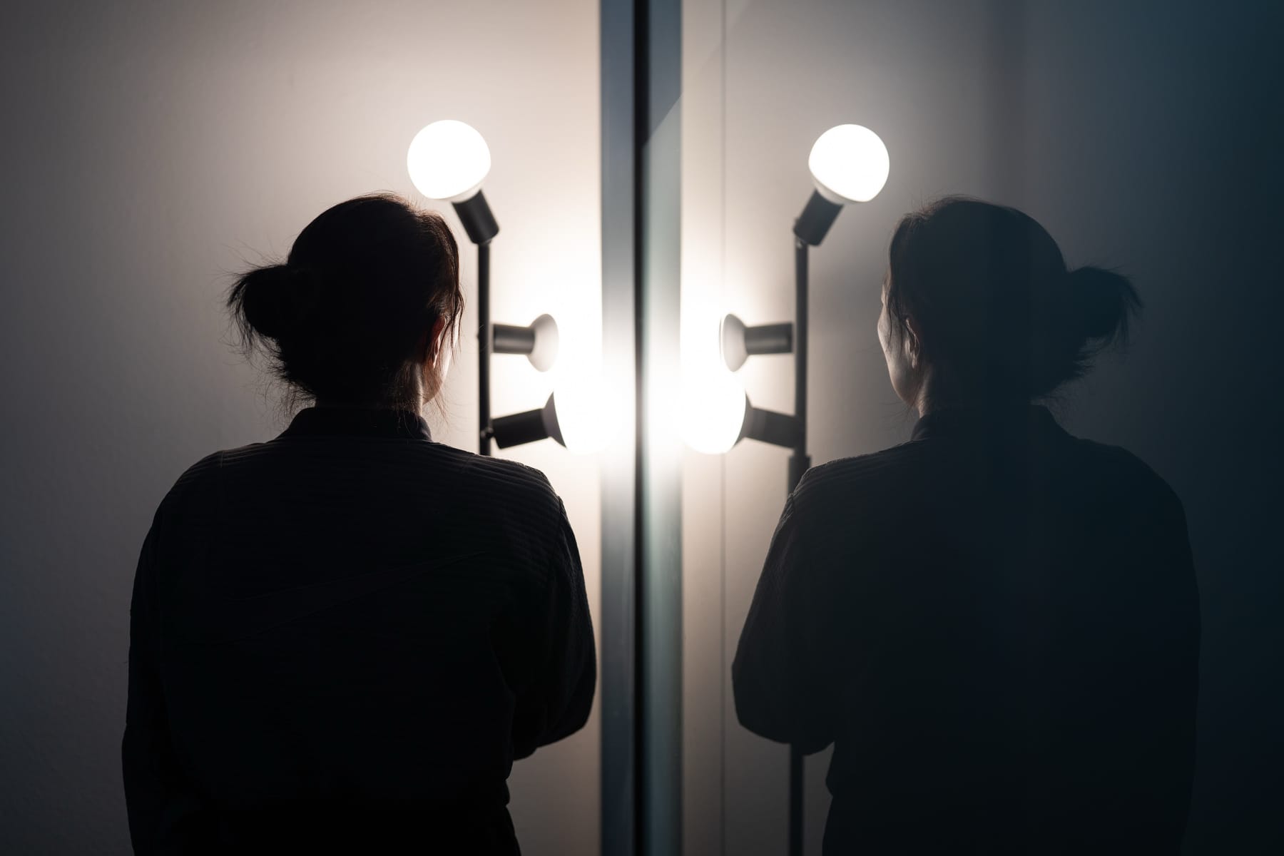 Woman standing with her back to the viewer in front of lamps.