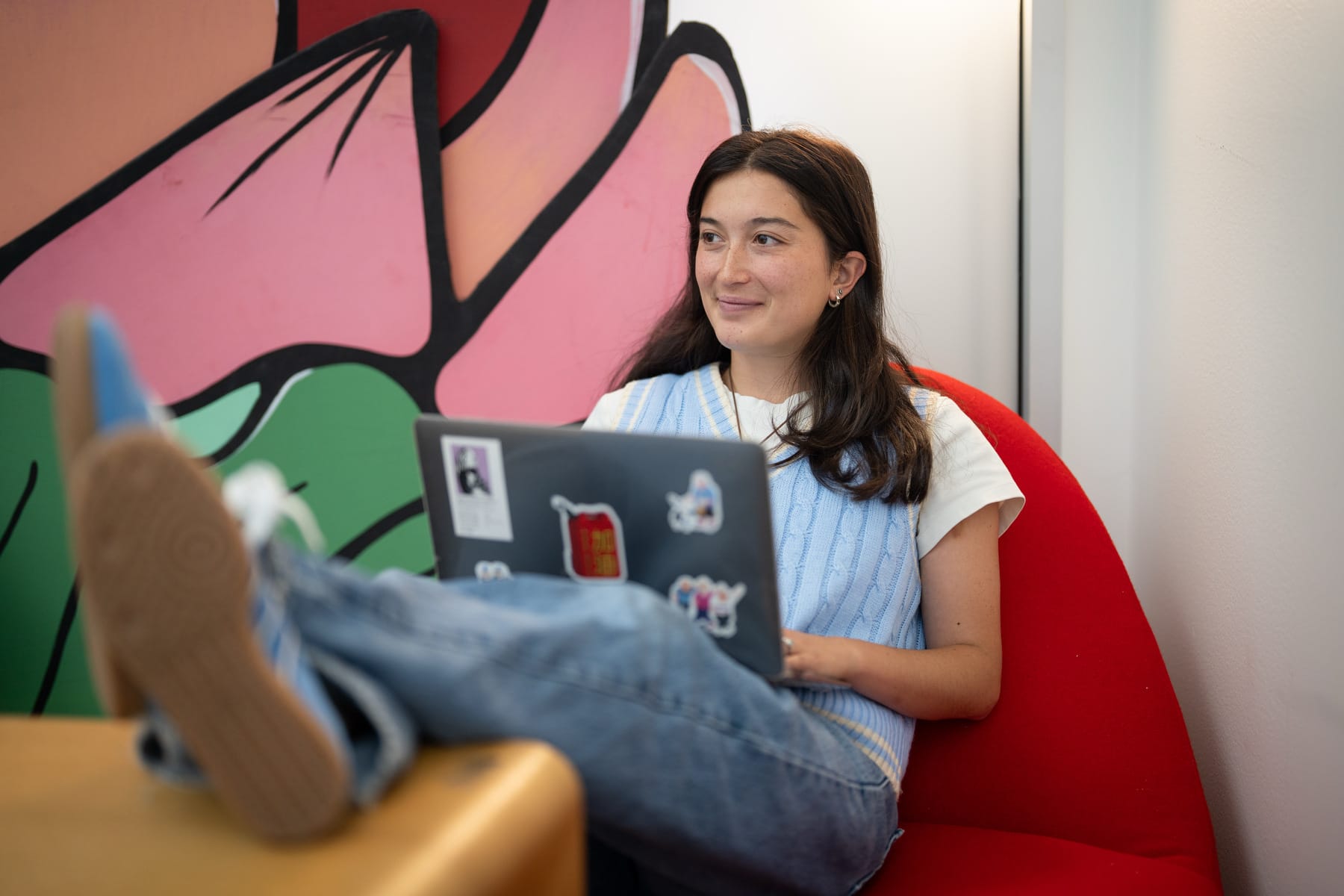 Woman with long hair sitting on a red chair with a laptop.