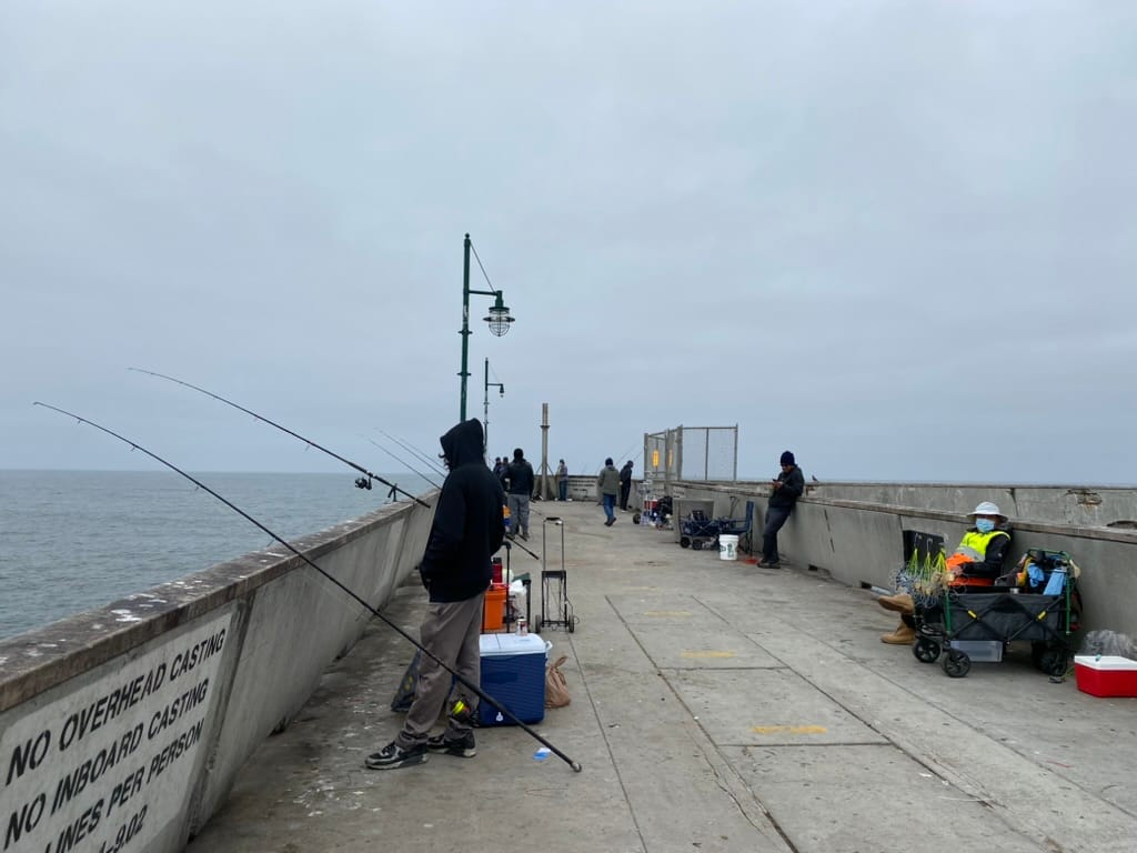 People fish and walk along the a pier that sticks out into the ocean