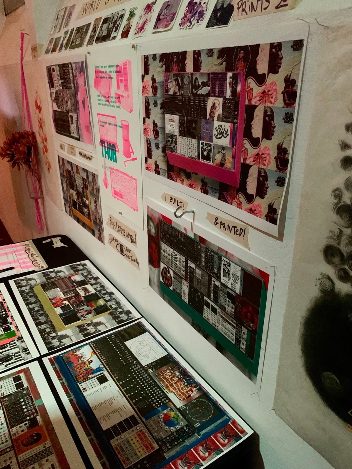 Photo of visual prints  arranged on a table and against a wall. Some show modular synths that collier built. 
