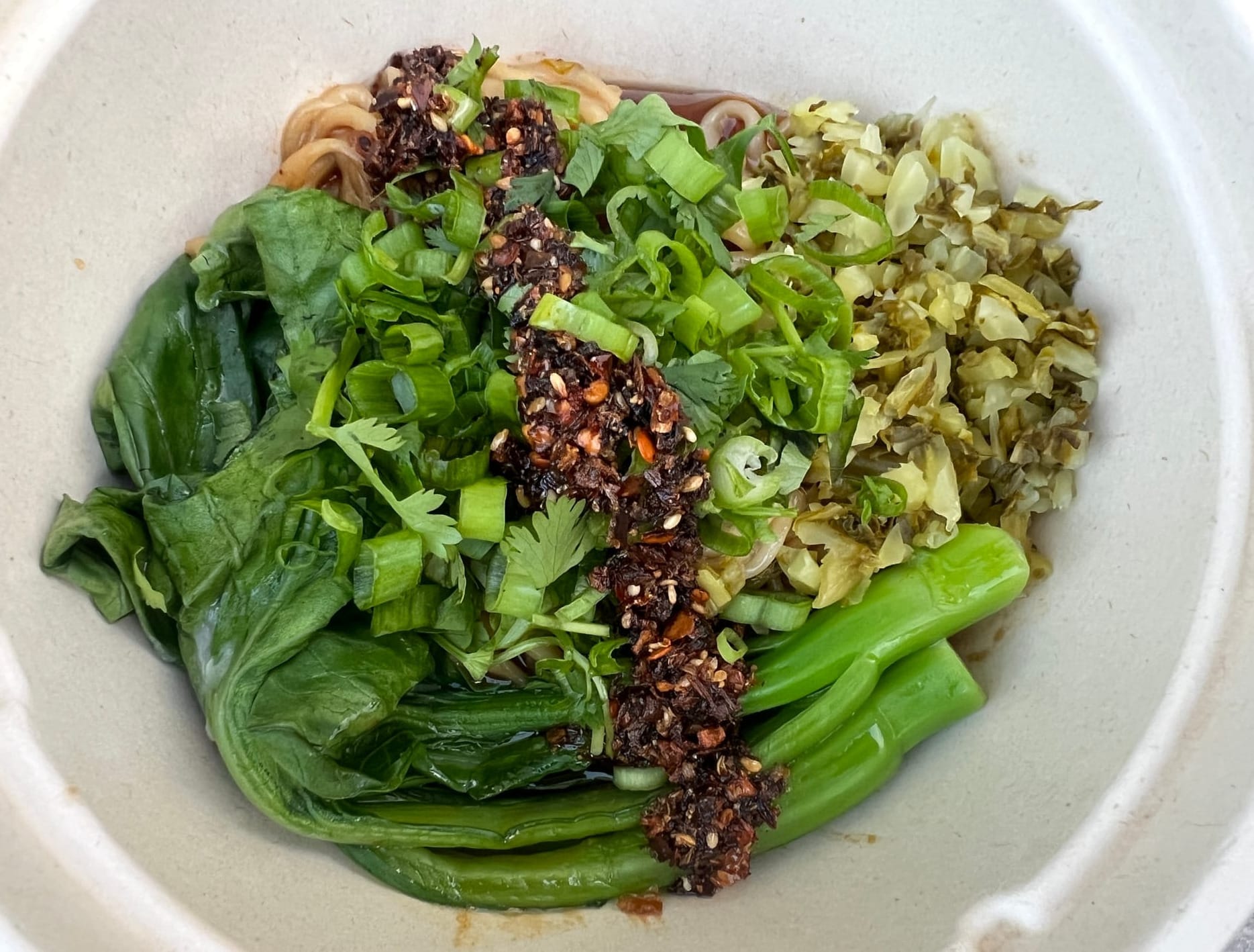 Noodles with greens, chili crisp, and scallions served in a compostable bowl
